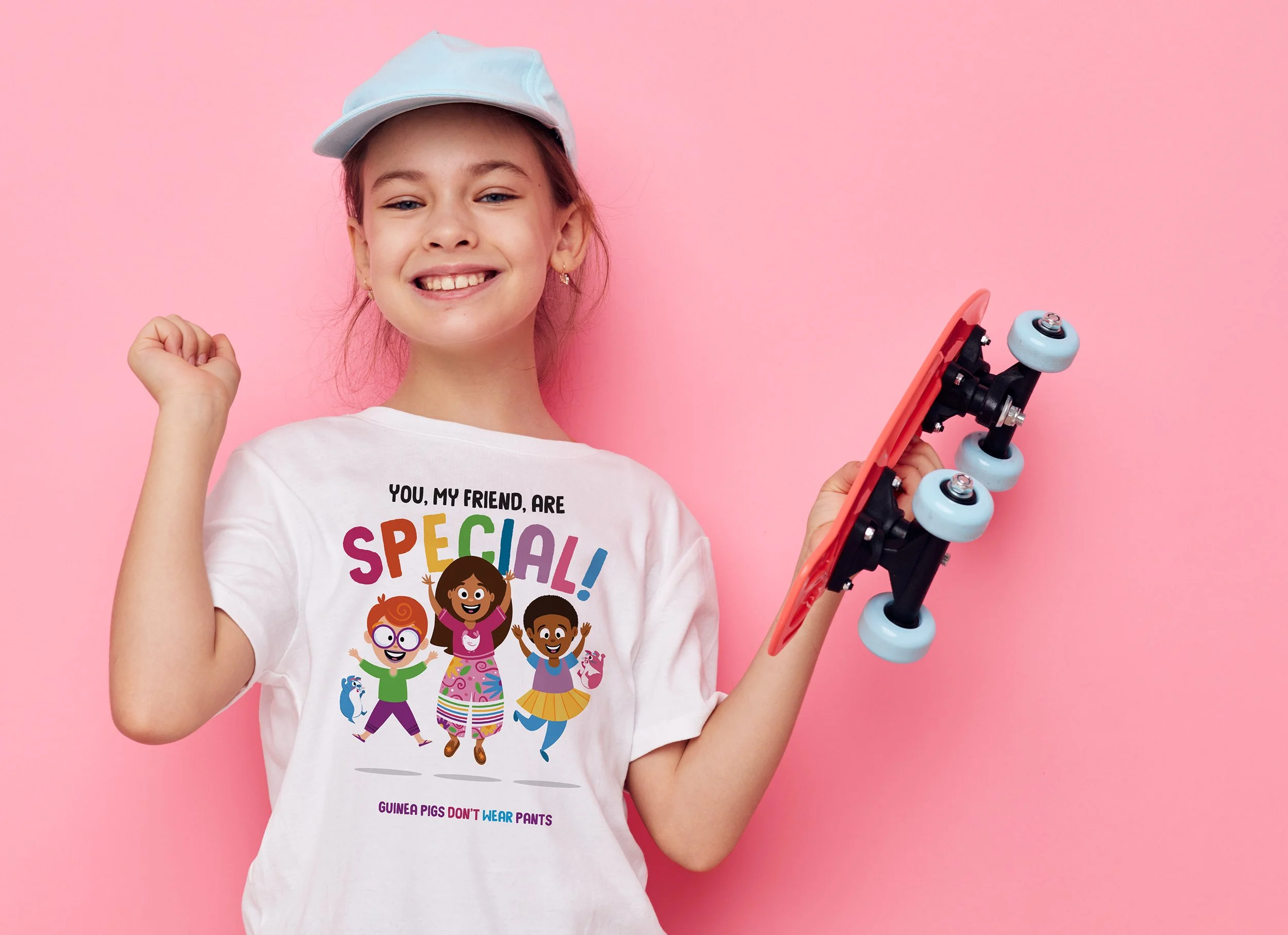 A young girl smiling and holding a skateboard, wearing a white T-shirt with colorful cartoon characters and text, against a pink background.