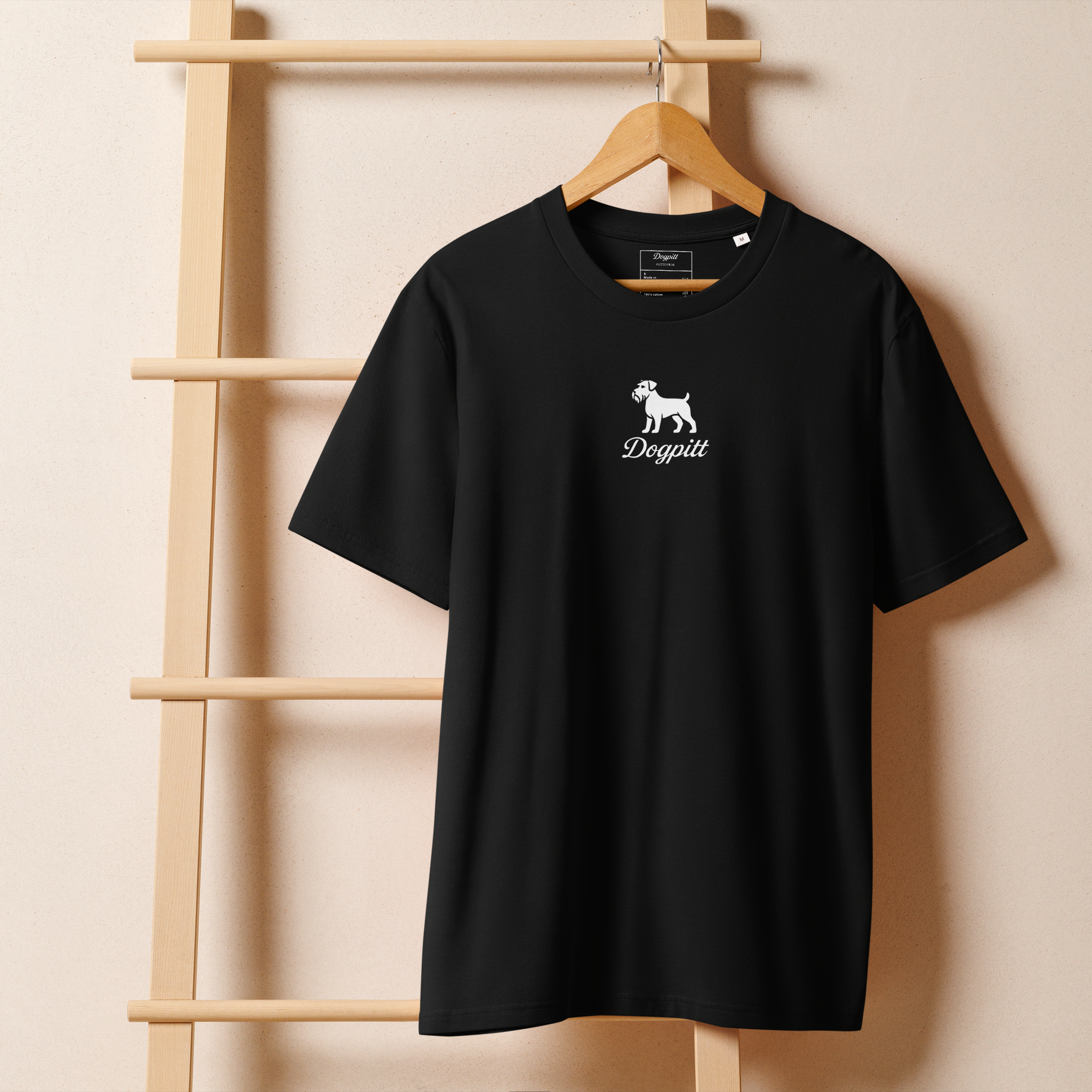 A black T-shirt hanging on a wooden hanger against a beige wall. The T-shirt has a white logo of a dog with the text "Dogpitt" beneath it.