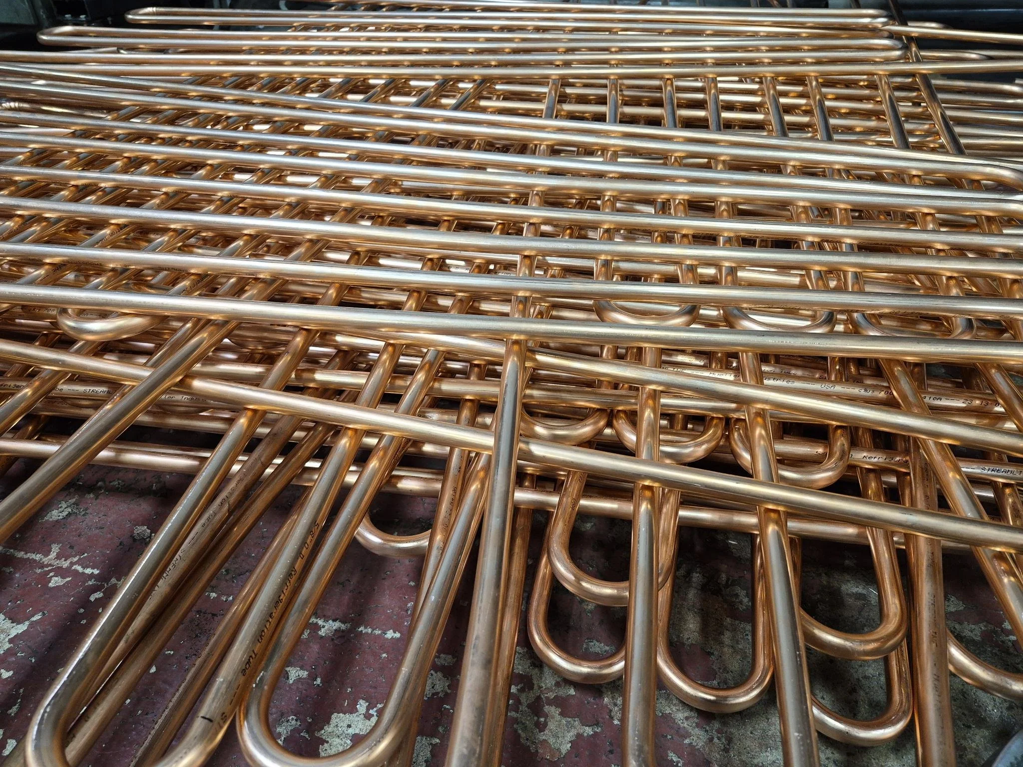 Stack of metallic copper-colored tubes or rods with hooks on one end, lying on a surface.