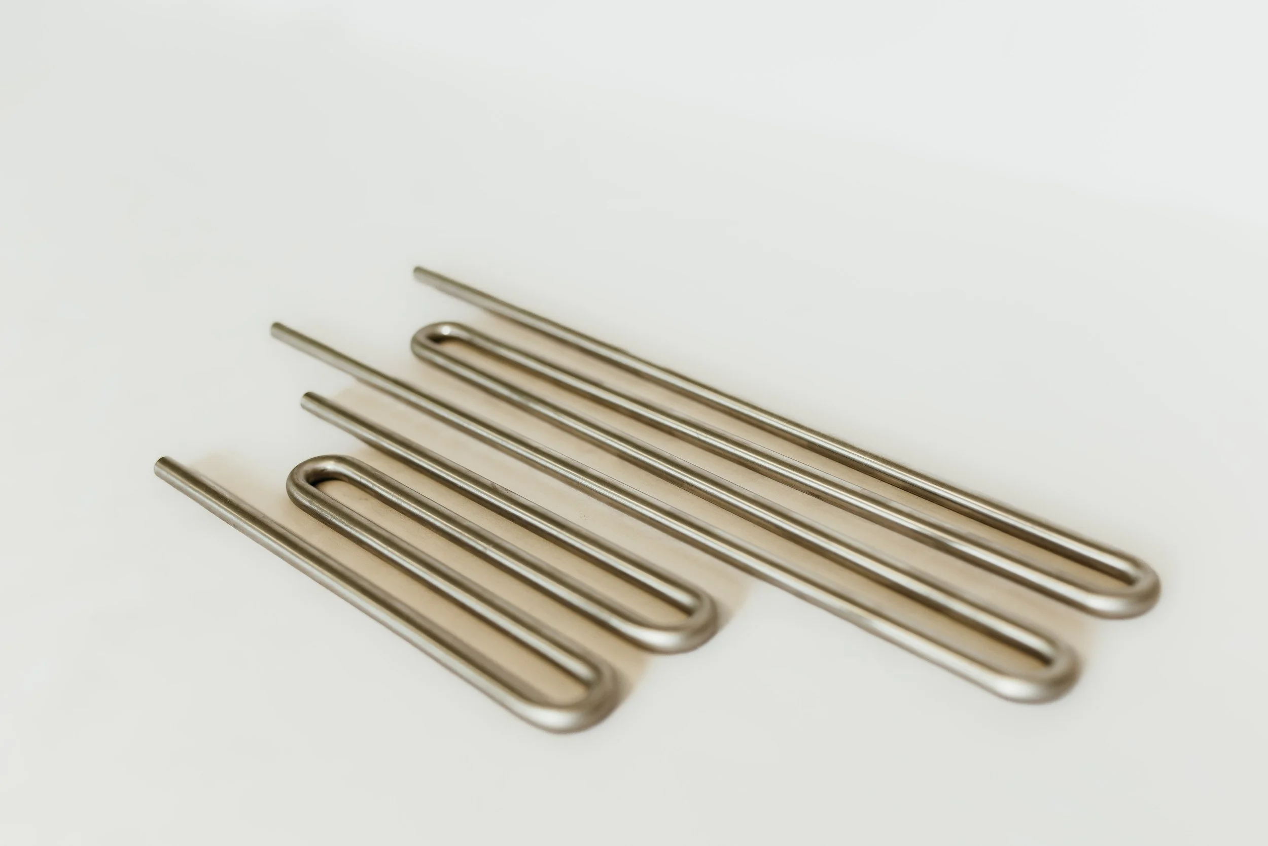 Two septentine stainless steel metal tubes with straight ends on a white surface.