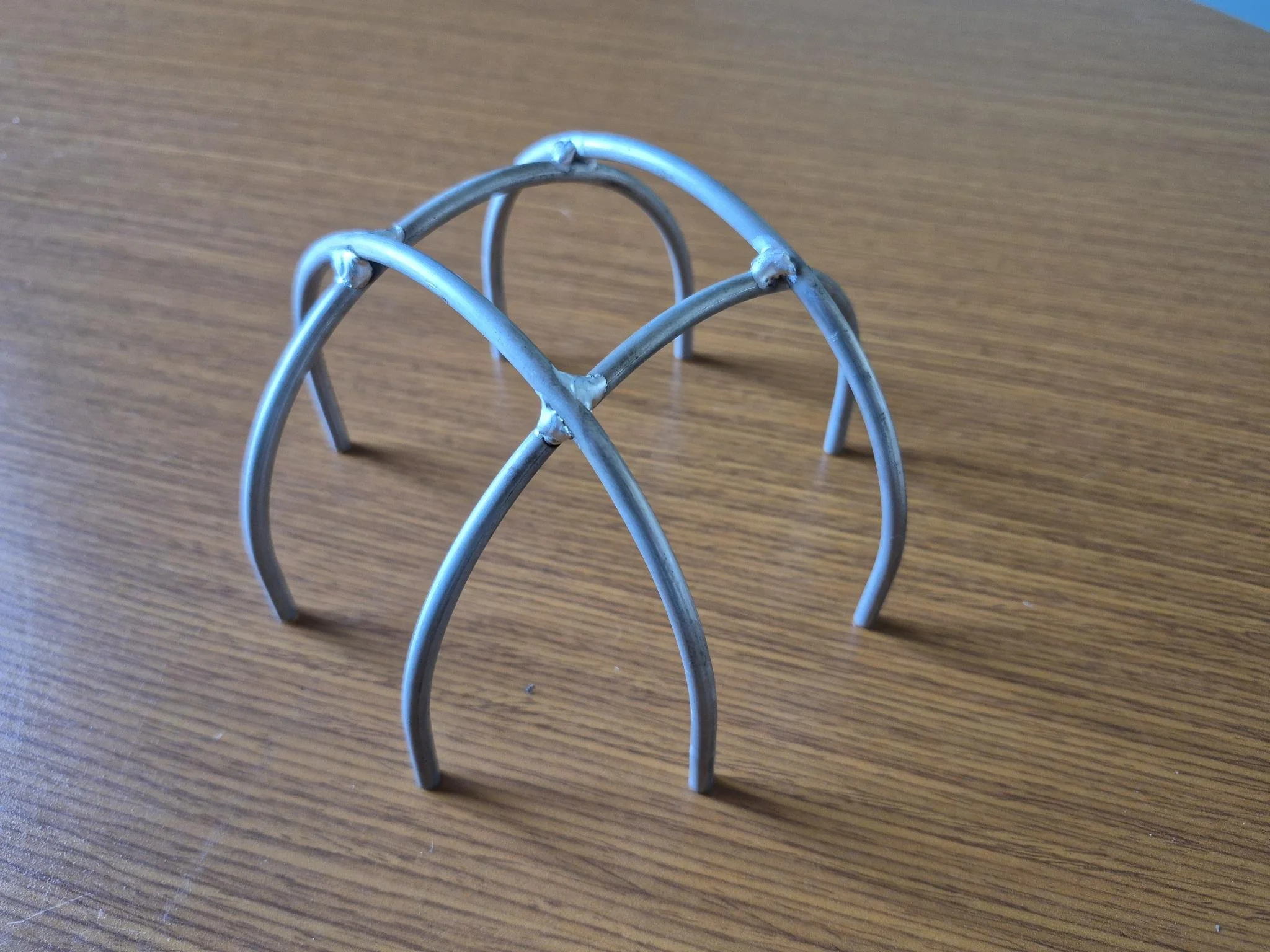A metal wire puzzle with a spherical shape, consisting of curved wires intersecting on a wooden surface.
