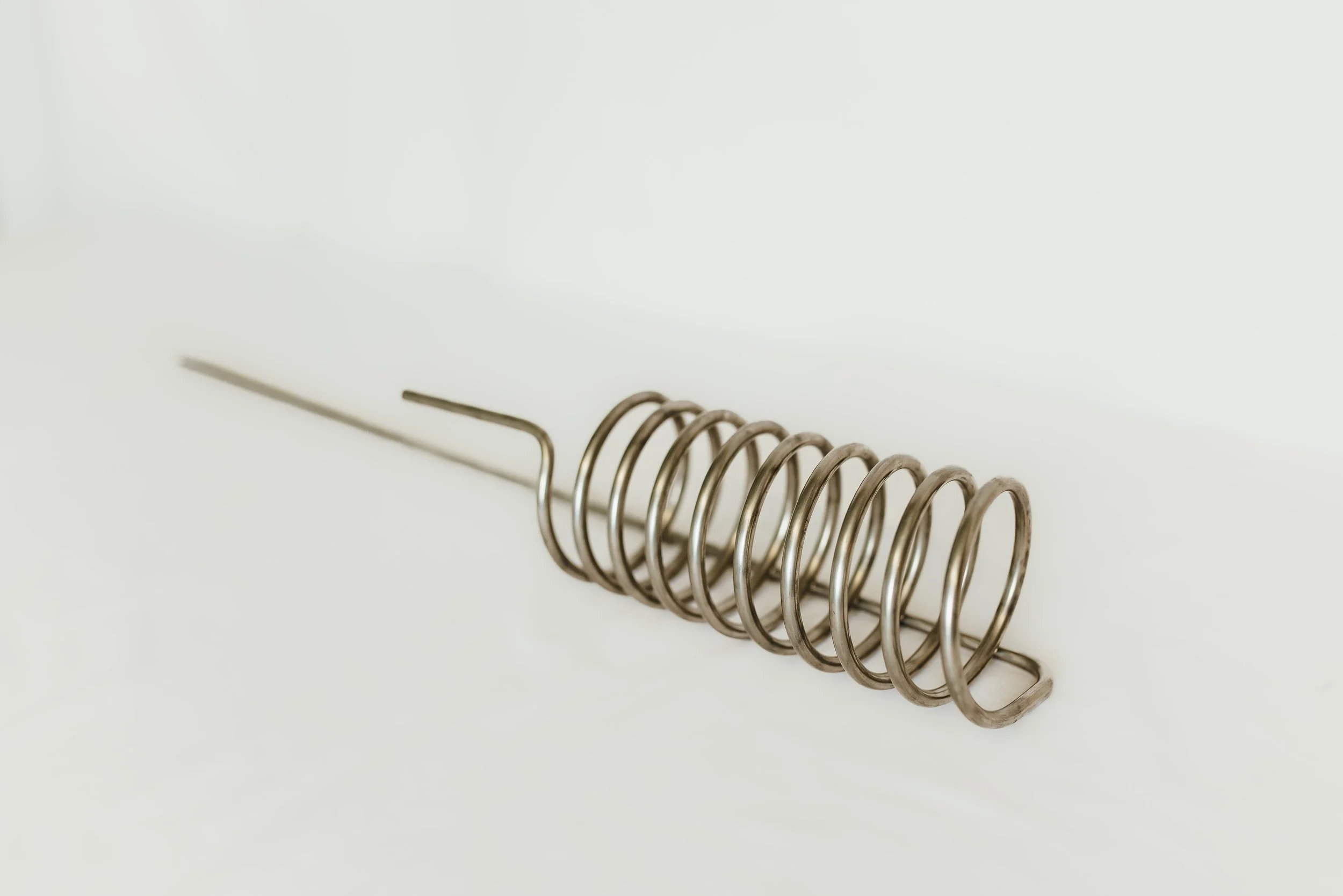 A stainless steel coil used for heat exchange. A spiral coil tube and a straight ends extending from one end, laid on a white surface.