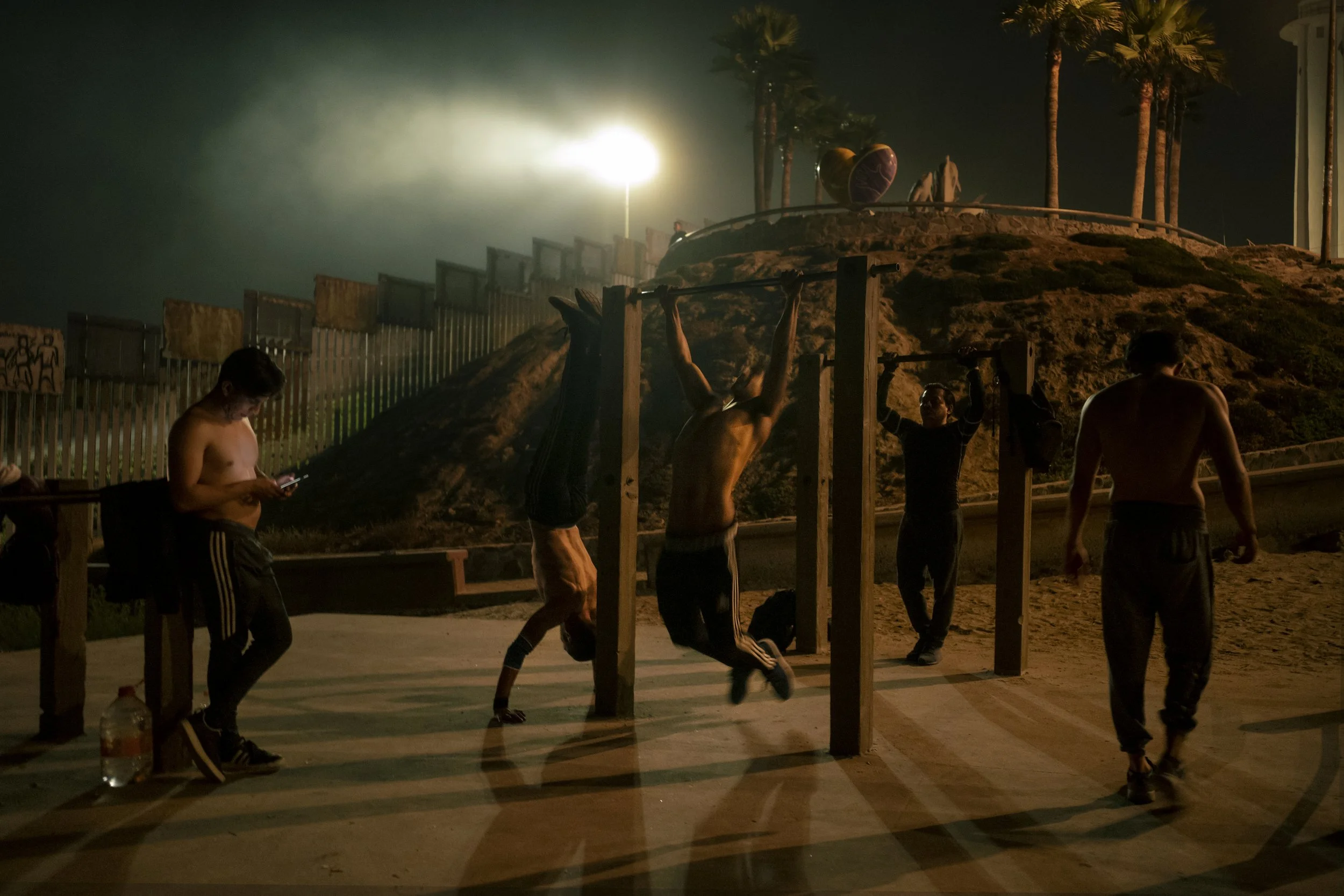 Tijuana, 2019. I took this image in the late evening, walking along the beach near the border. The coastal mist was thick, and the scene felt immediately cinematic. I was drawn to this group of young men working out near the wall. I walked right up t