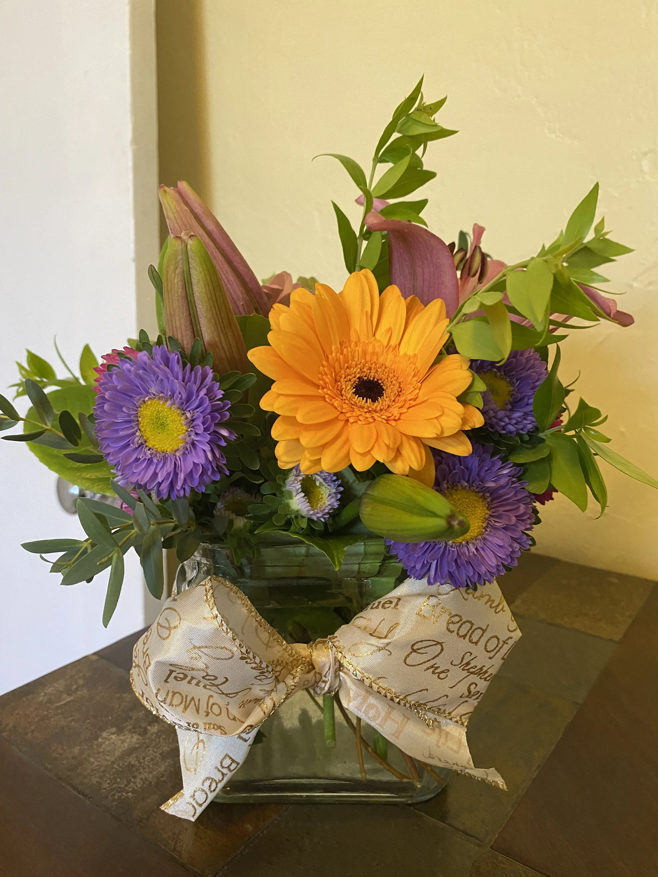 Colorful flower arrangement in a glass vase with a cream-colored ribbon bow.