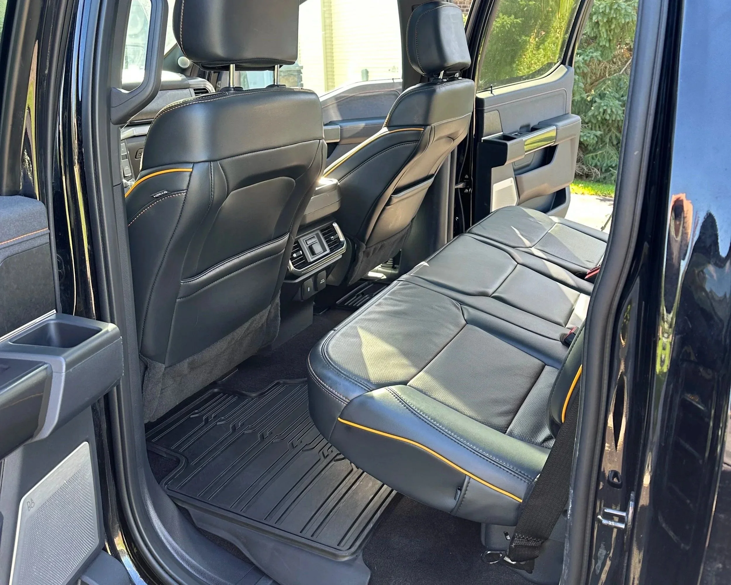 Interior of a modern vehicle with black leather seats, including the back seats and front seats, with a view of the outdoors through the windows.