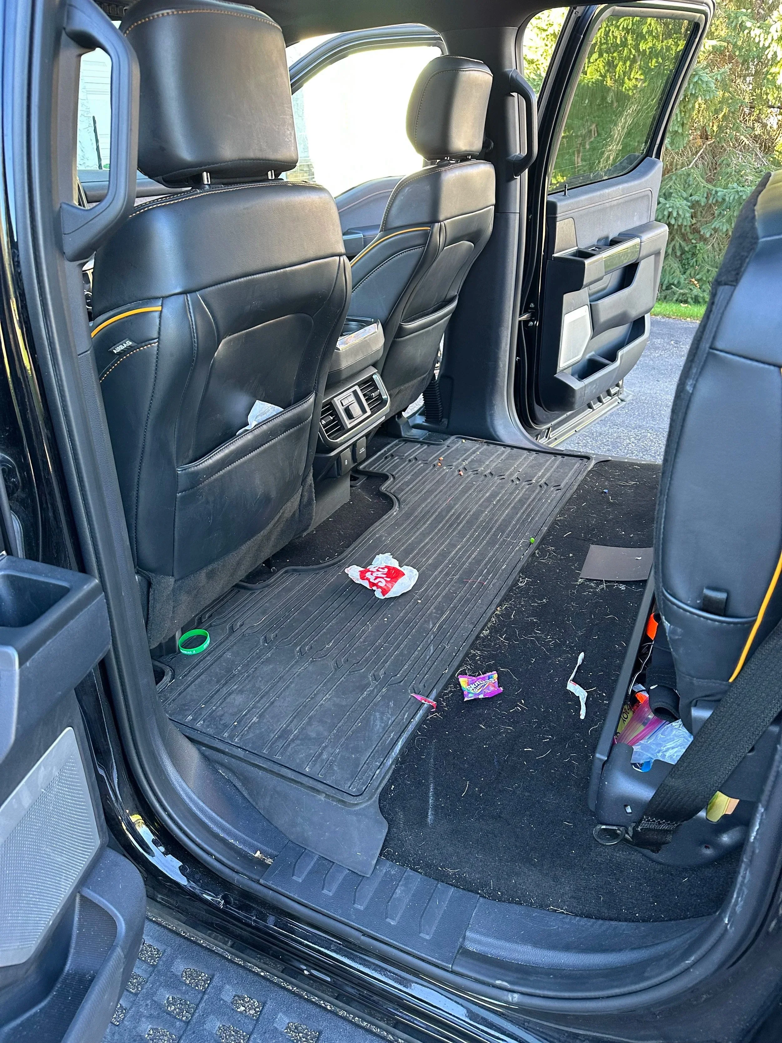 Interior view of a vehicle's backseat area with trash on the floor, including a candy wrapper and other debris.