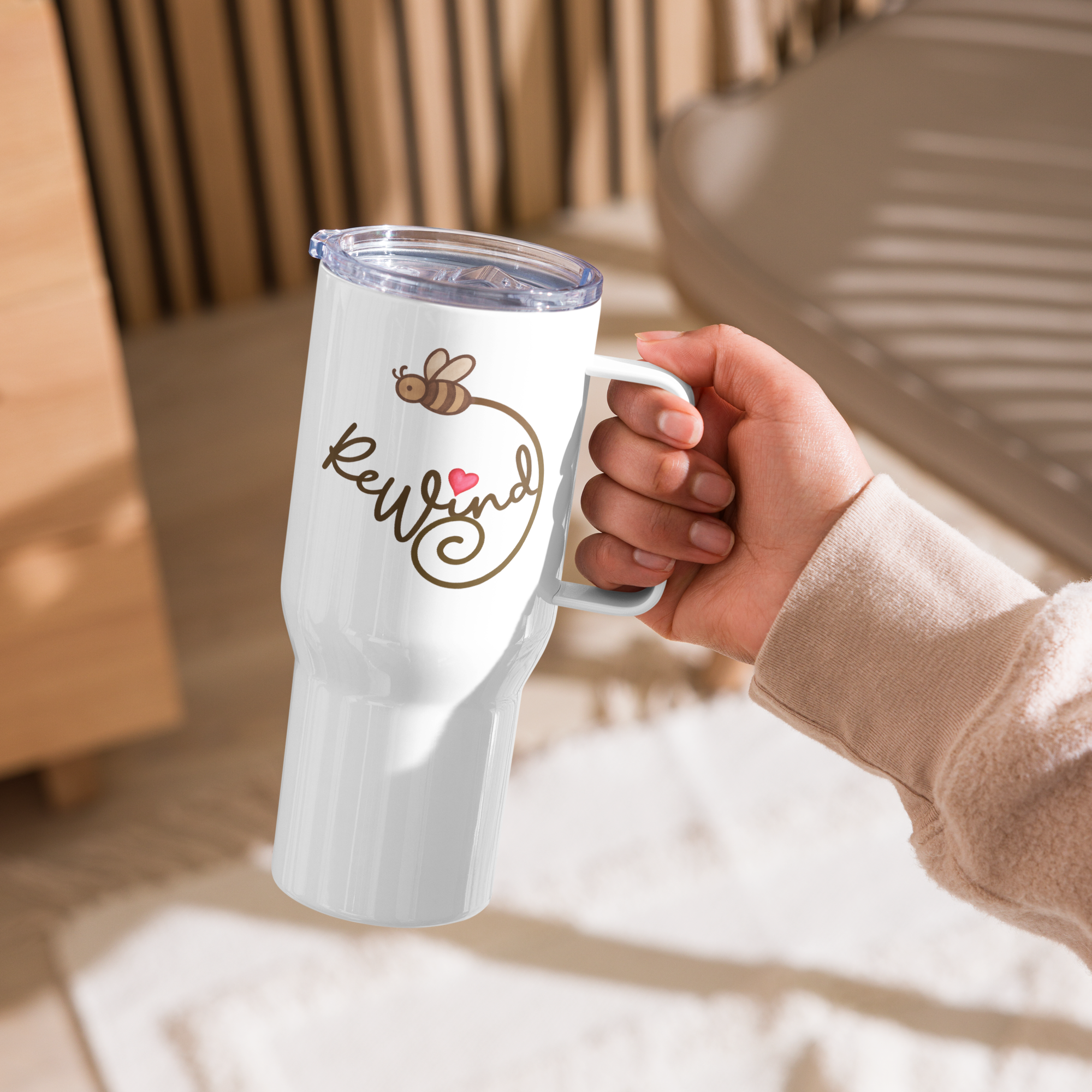 Lifestyle: hand holding 25-oz white travel mug—ReWind script with bee trail.