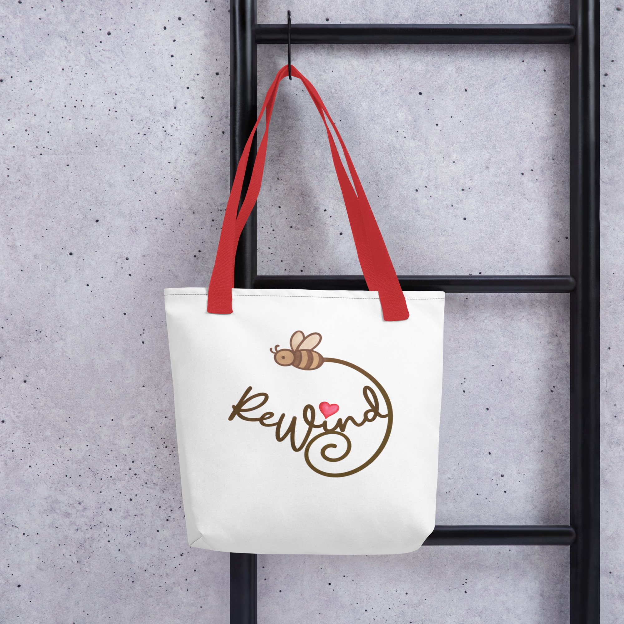 Red-handle tote hanging on concrete wall—ReWind bee-trail logo.