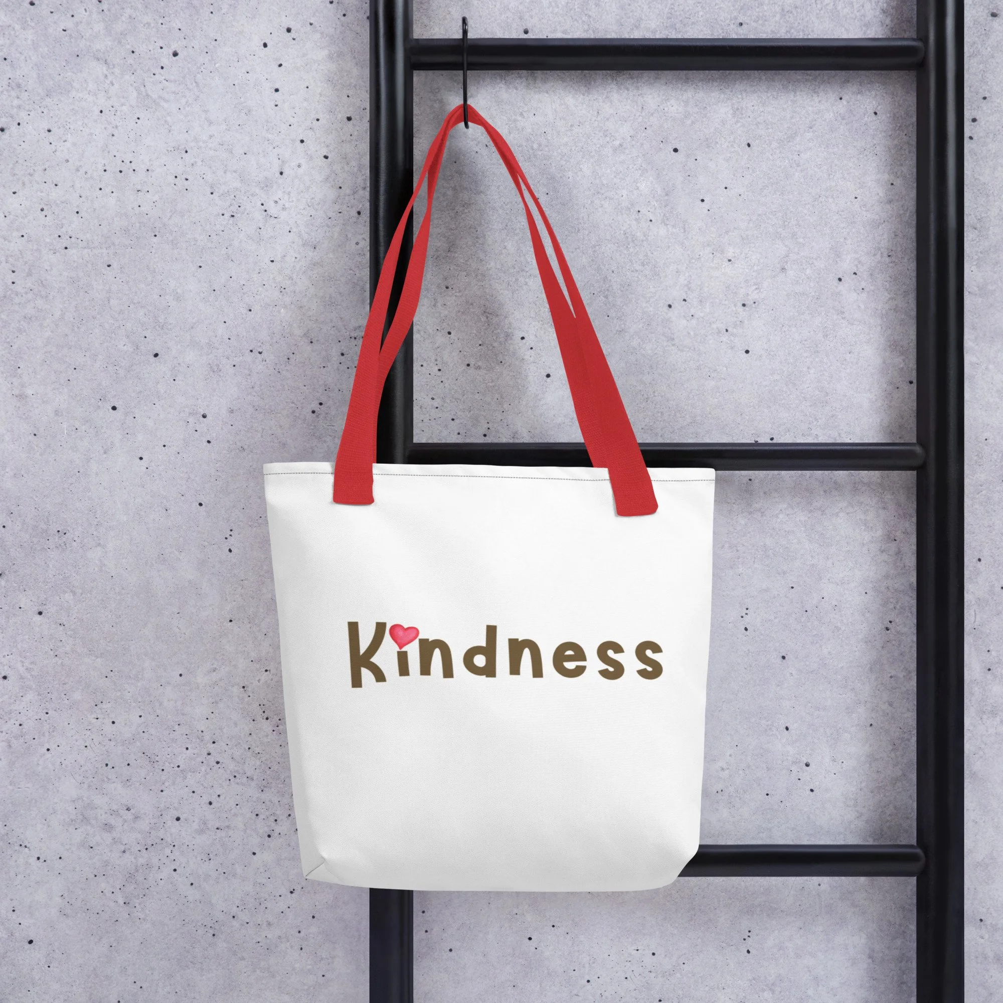 Red-handle tote hanging on concrete wall—“Kindness” wordmark.