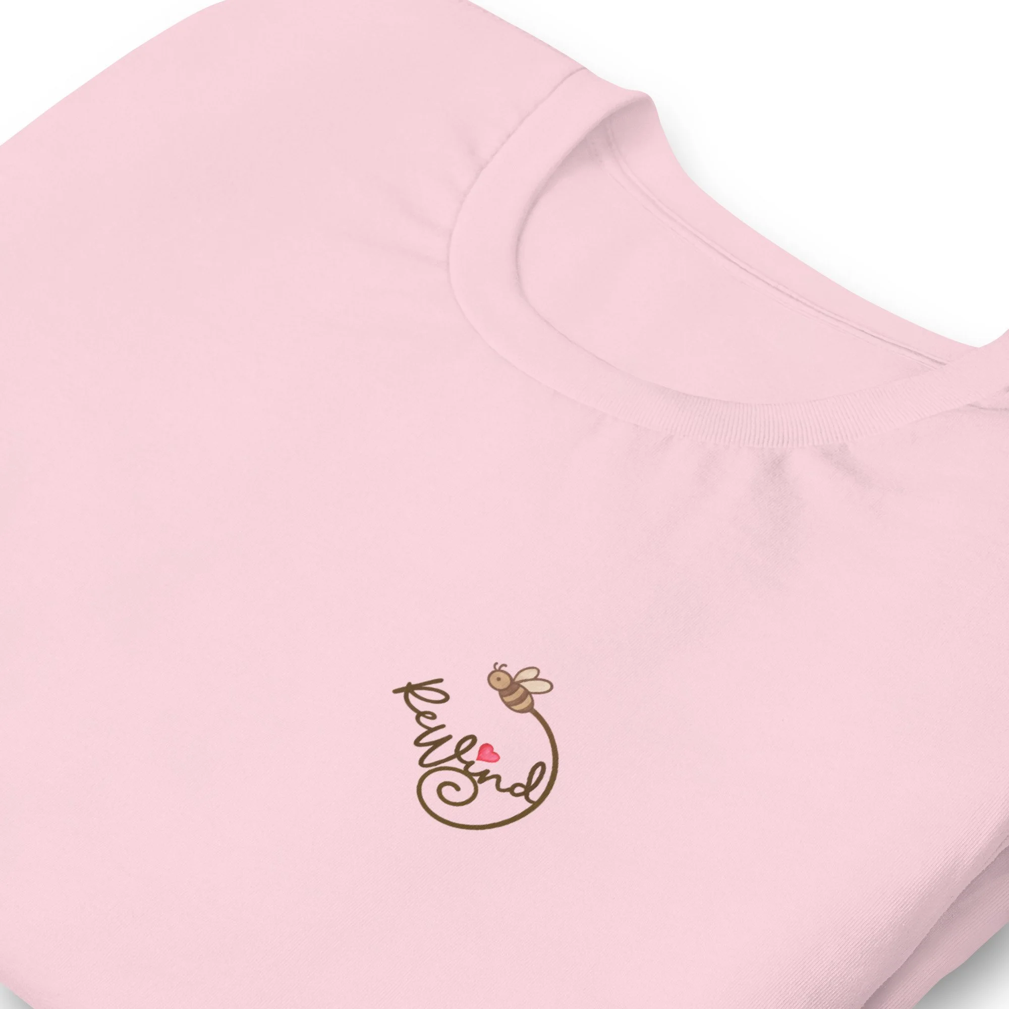 Unisex t-shirt, soft pink, folded view — front with ReWind bee-and-heart logo and back with “Kindness” text (heart over the i).
