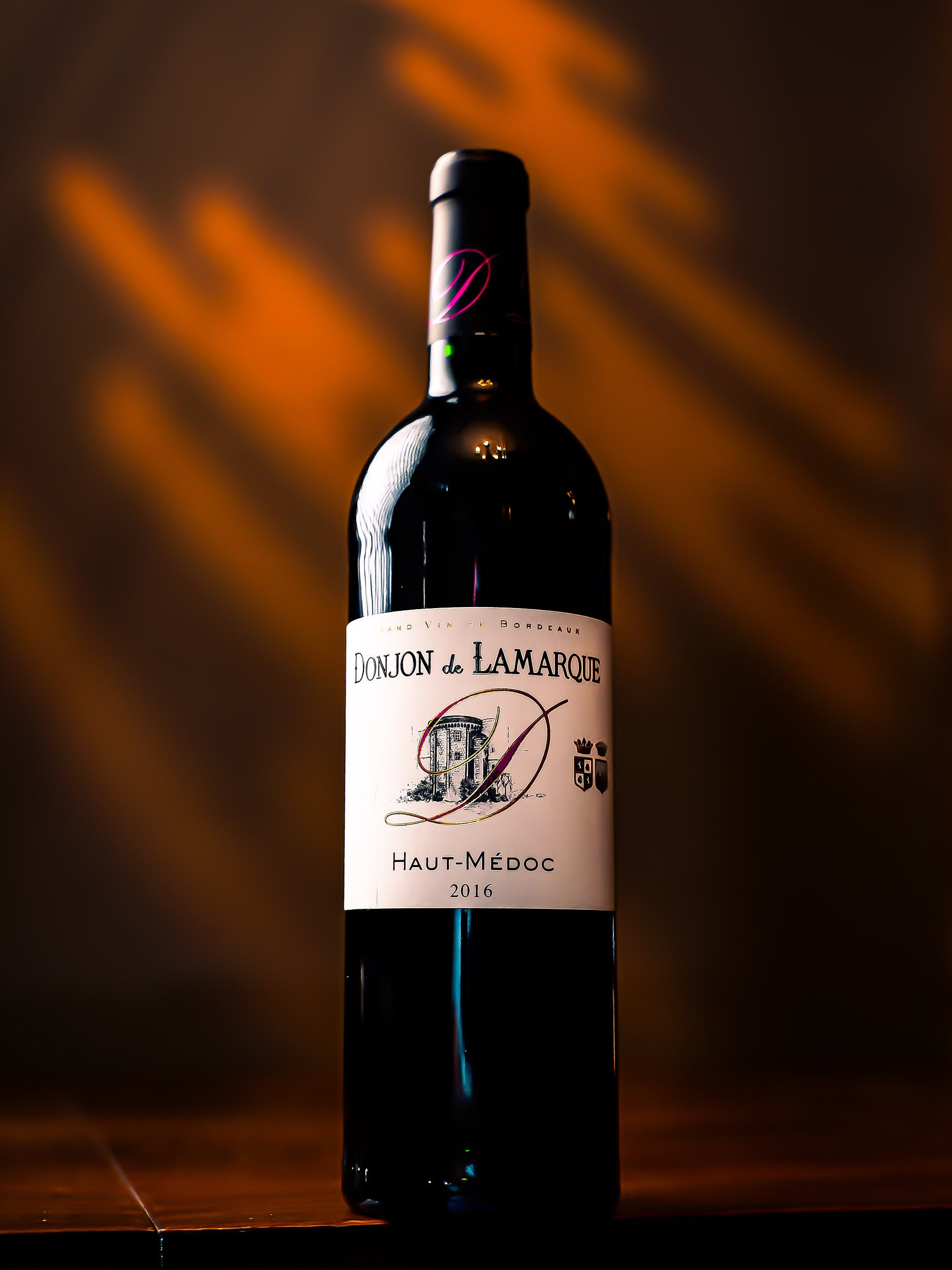 A bottle of Donjon de Lamarque Haut-Médoc red wine from 2016 standing on a wooden surface with a dark blurred background.