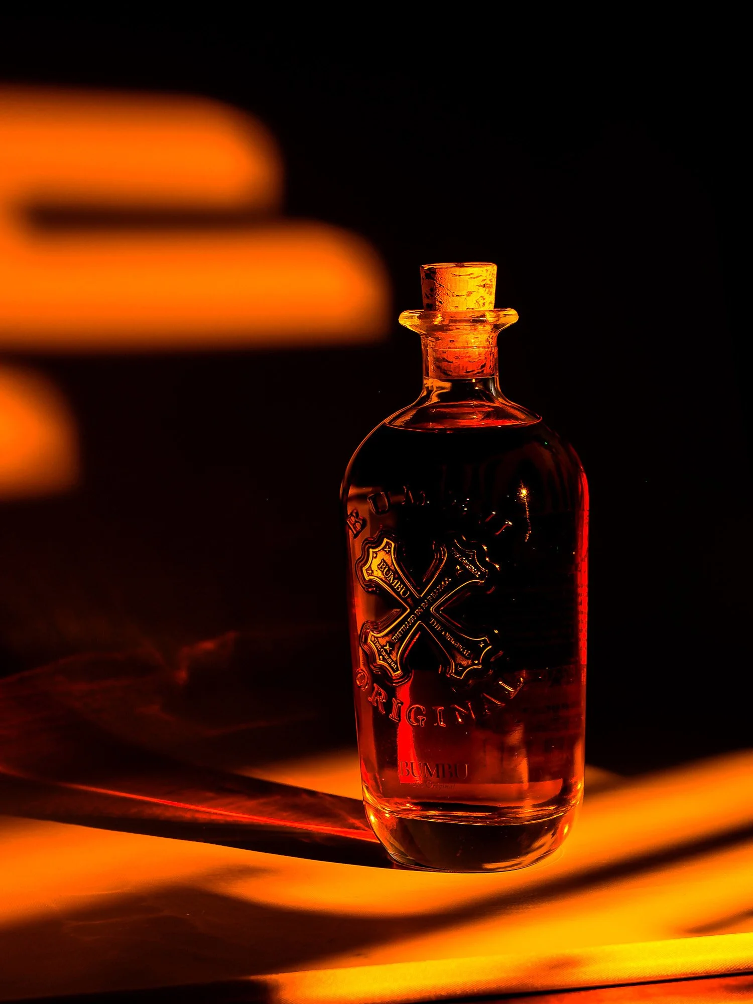 A small glass bottle with a cork stopper, illuminated by warm, reddish-orange light, casting a shadow on a glowing surface with a dark background.