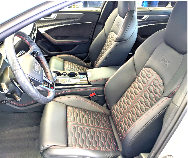 Interior of a sporty car with leather seats featuring red accent stitching, a steering wheel with an Audi logo, and a center console with cup holders.