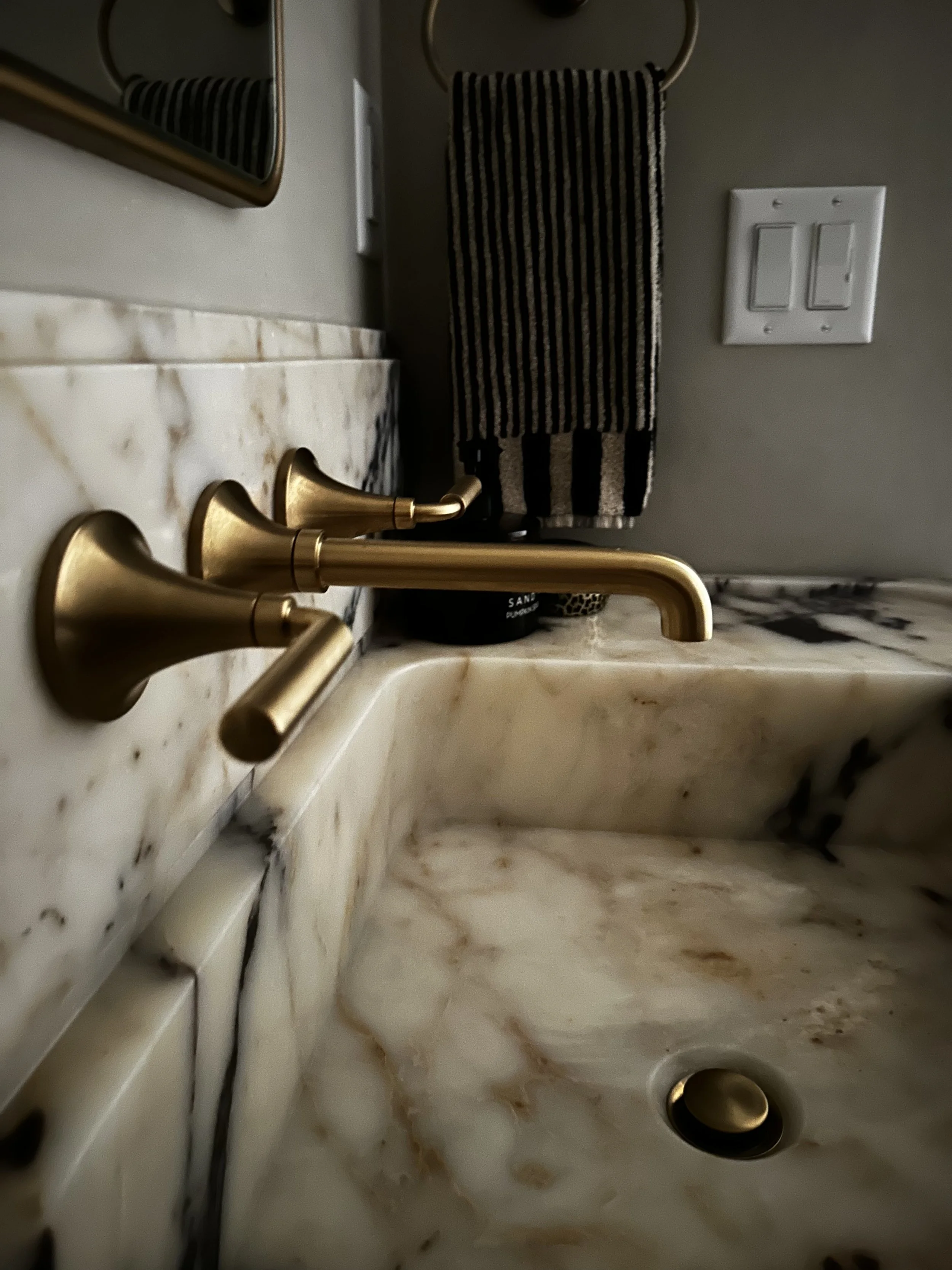 gold wall mounted brass faucet, custom calacatta violi marble vanity, cream and black striped towel, gold mirror, modern organic, limewash walls, interior design, bathroom renovation