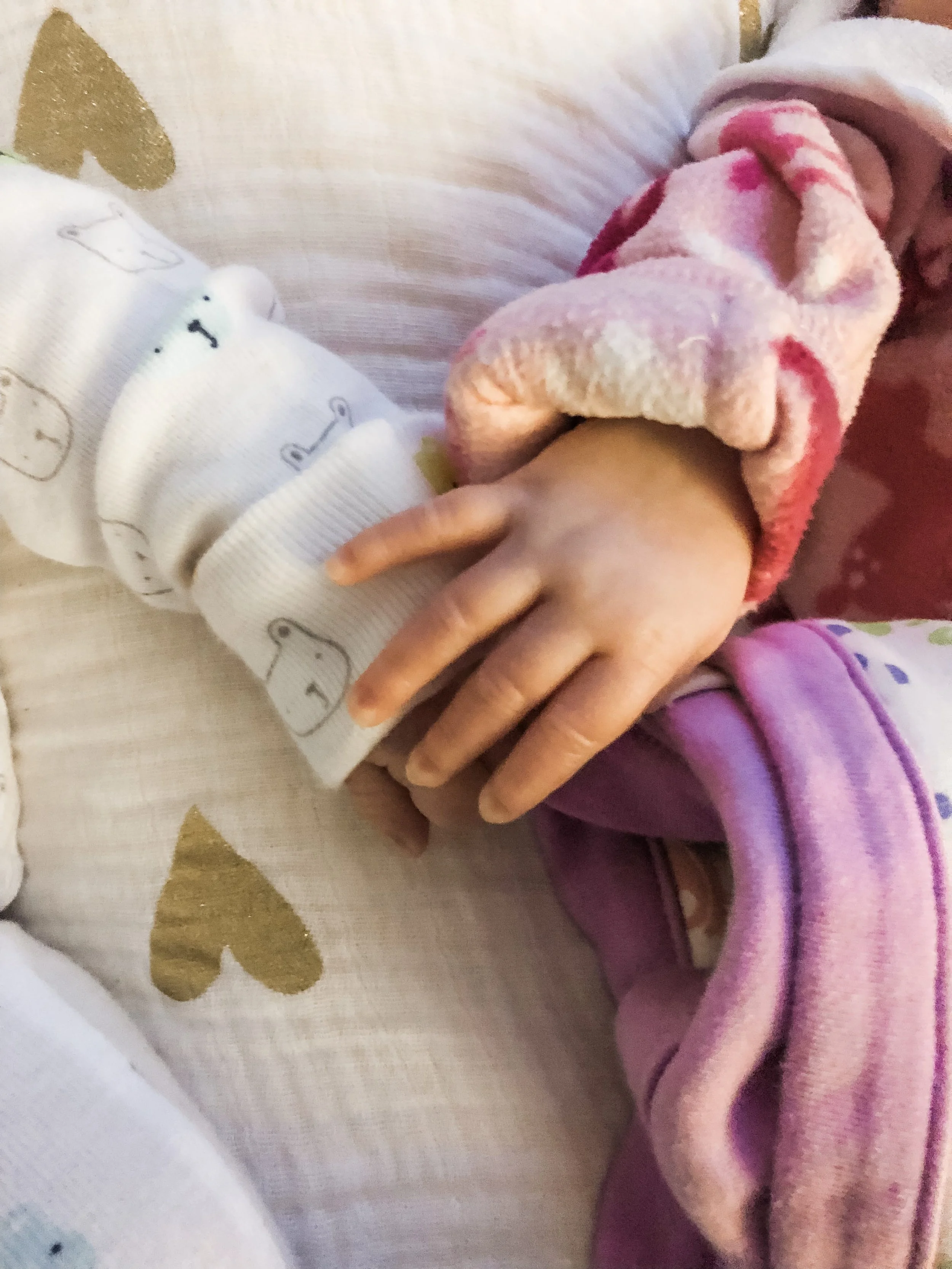 Close-up of two children's hands holding each other, one wearing a pink fleece jacket and the other wearing a white sleeve with bear faces.