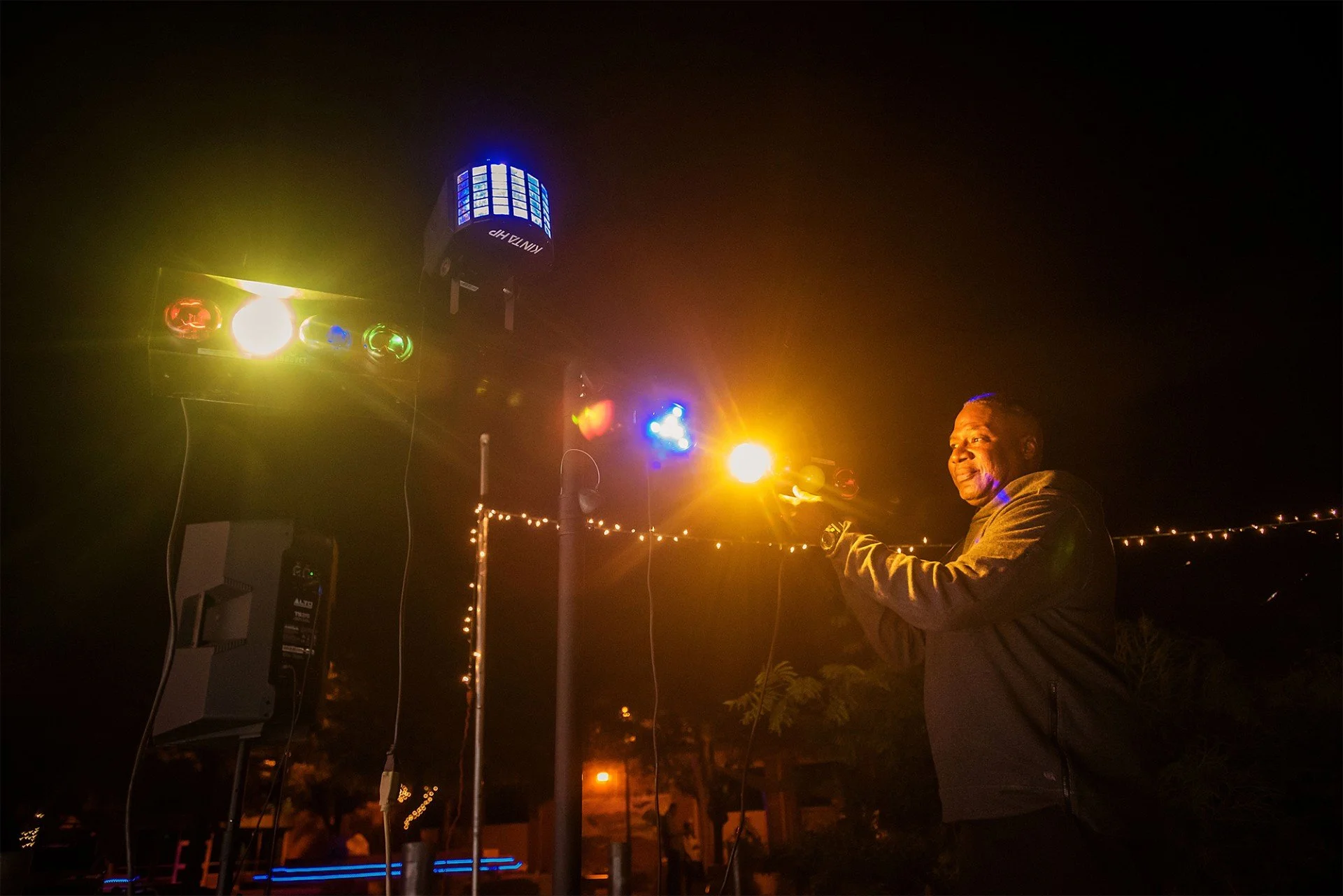 A man at night holding a control device with colorful stage lights in the background.