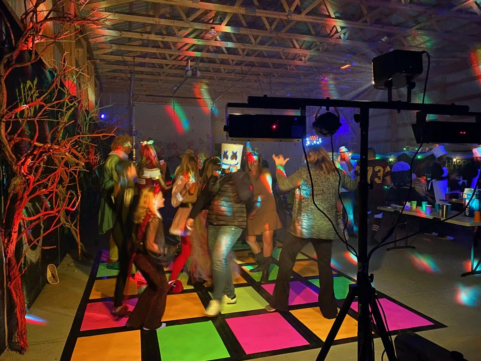 People dancing on a colorful lit dance floor at a party with disco lights, surrounded by party decorations and tables.