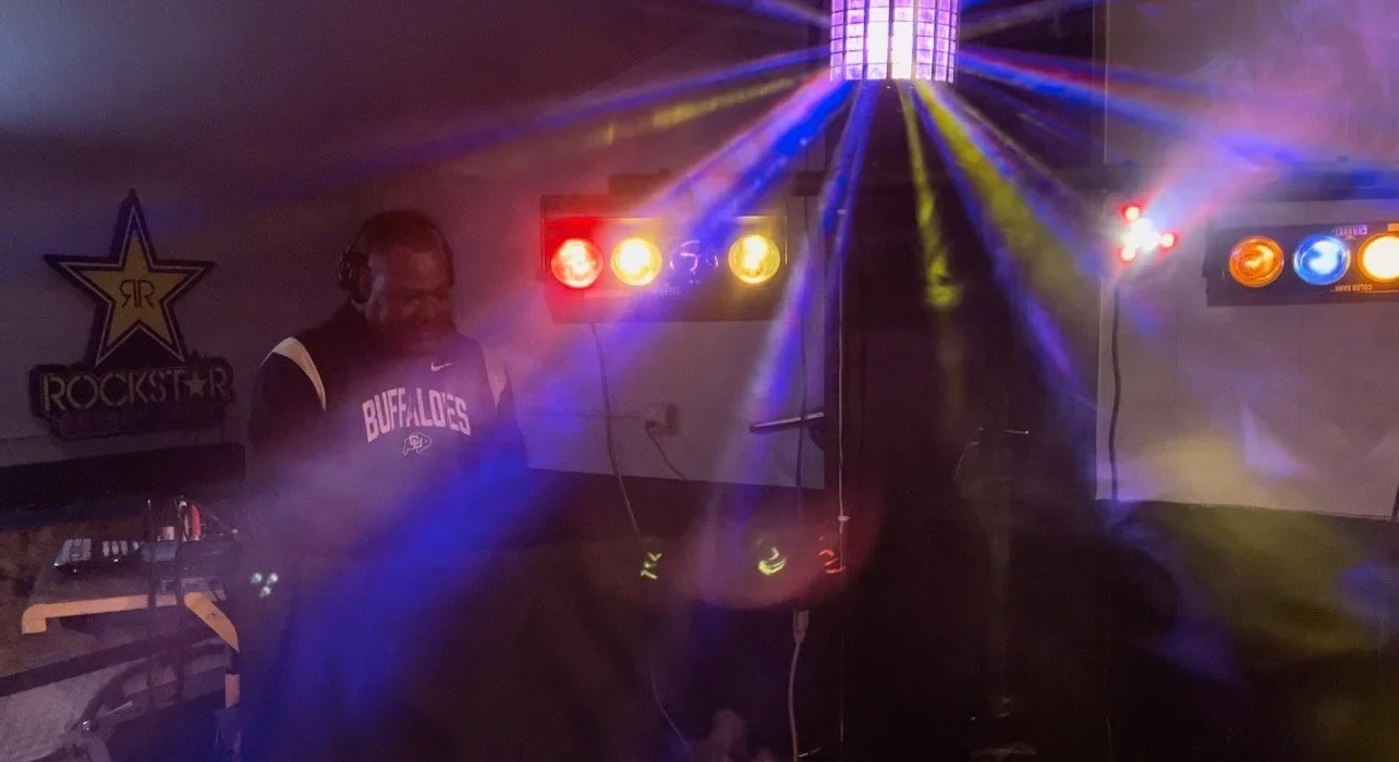 A person wearing a dark basketball jersey with 'Buffaloes' written on it, standing in front of colorful stage lights and DJ equipment.