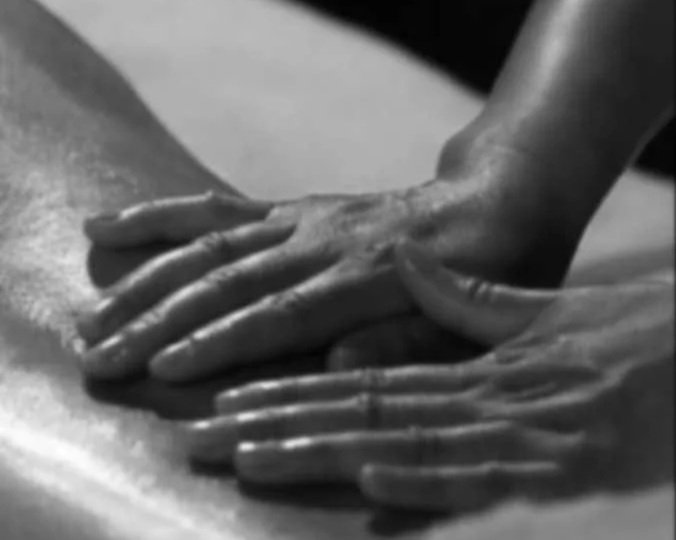 Mãos de uma pessoa fazem massagem ou aplicam alguma técnica sobre a pele de uma pessoa deitado, possivelmente em um tratamento de massagens ou cuidados com o corpo.