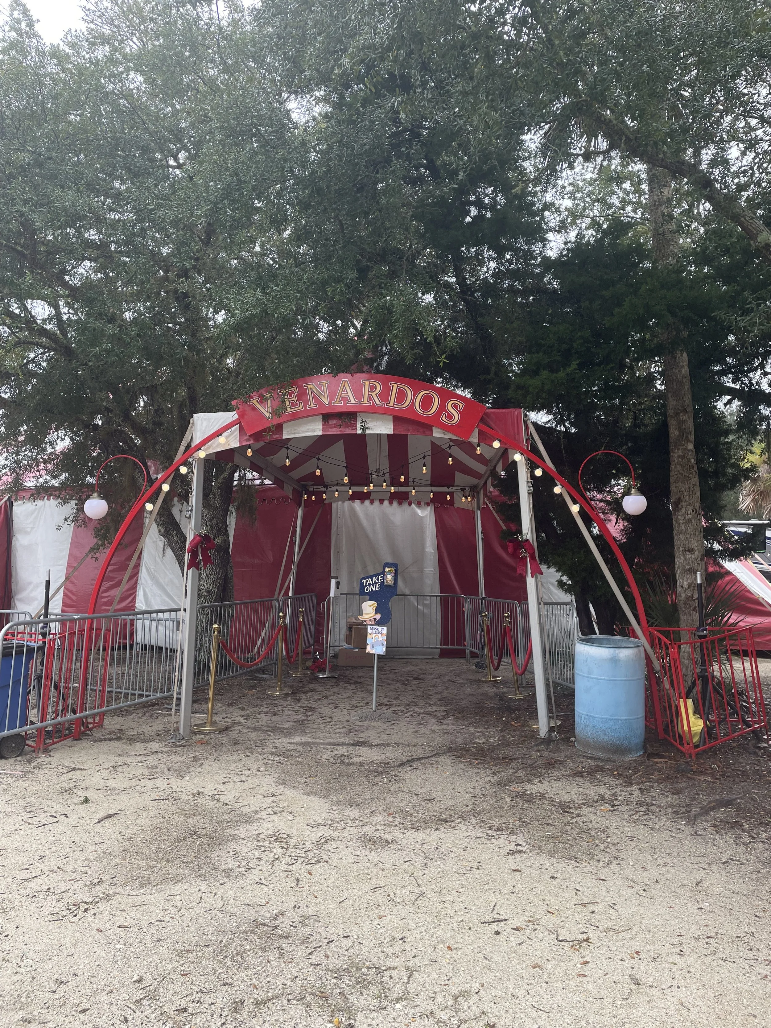 Circus tent with red and white stripes labeled 'Venardos' at entrance, surrounded by trees and fencing.