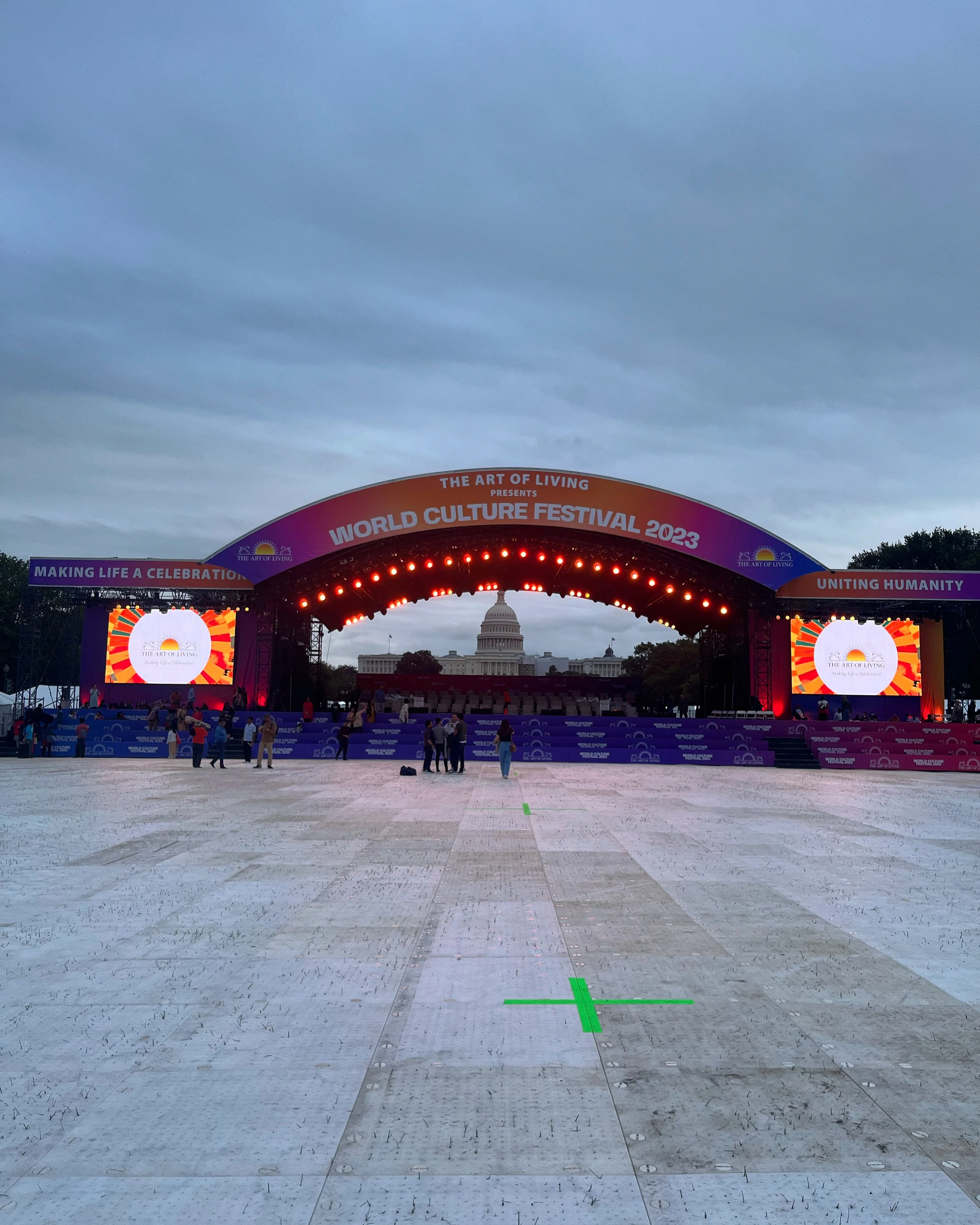 Stage set up in front of the U.S. Capitol building for the World Culture Festival 2023, with people gathering and preparing as evening falls.