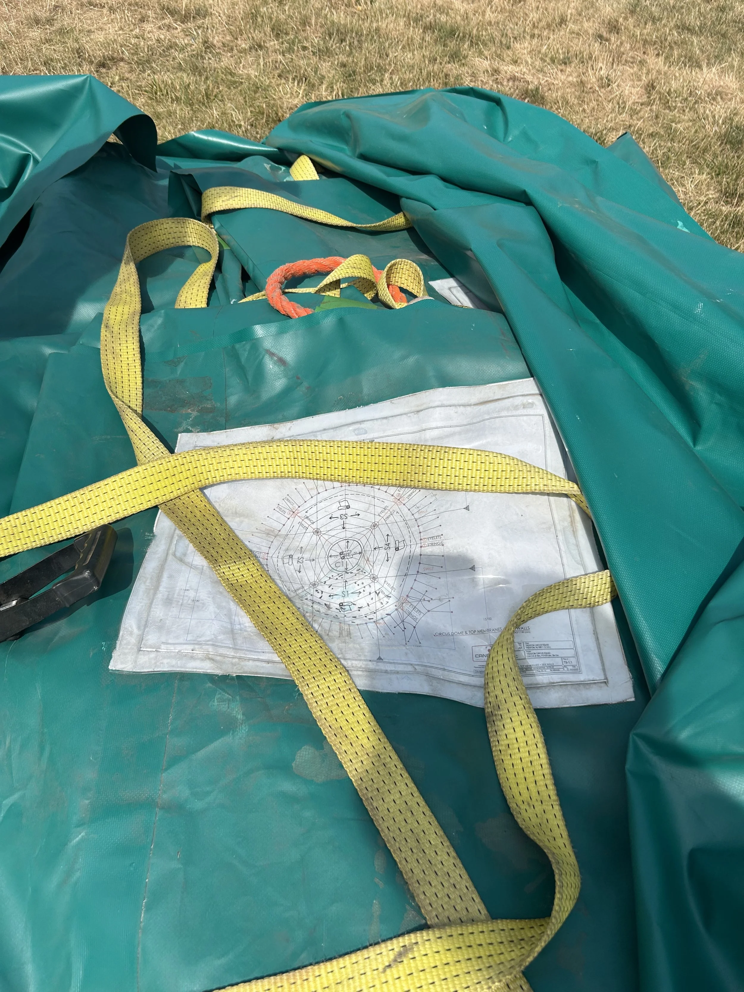 A close-up of a green inflatable structure with yellow straps, and a mechanical or technical diagram underneath on a grassy surface.