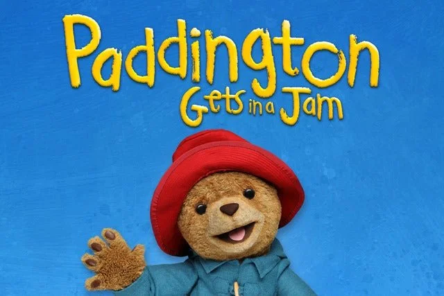 Cover of the children's book "Paddington Gets in a Jam" featuring Paddington Bear wearing a red hat and a blue coat, waving.