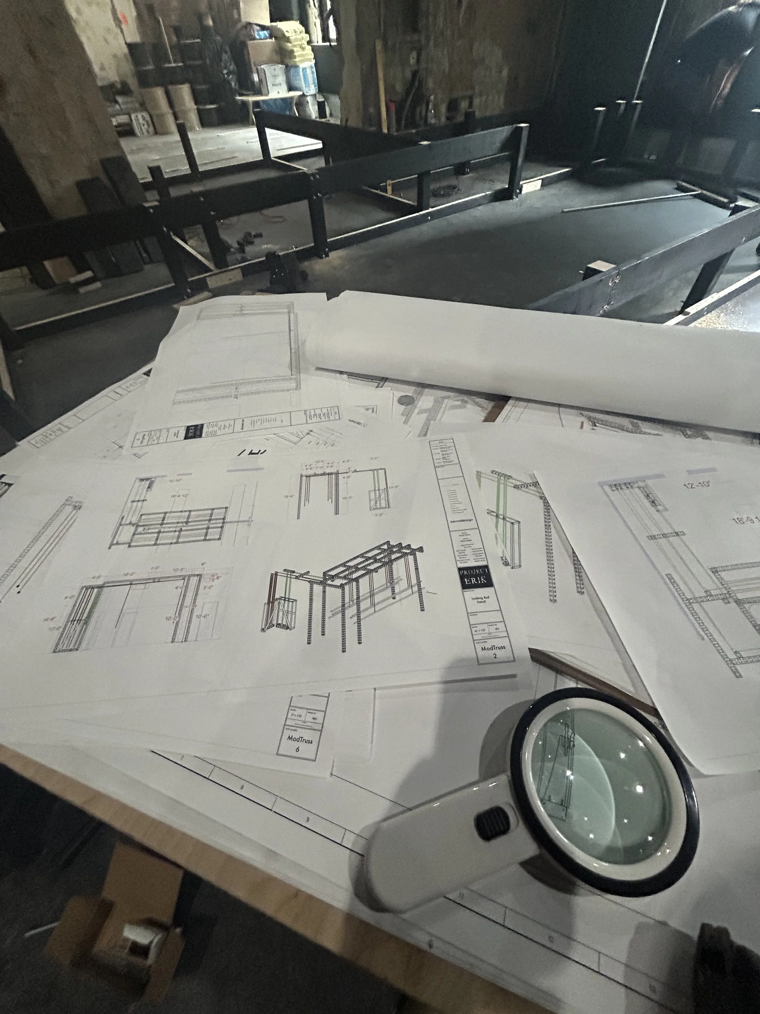 Blueprints and a magnifying glass on a worktable in a workshop or construction site.