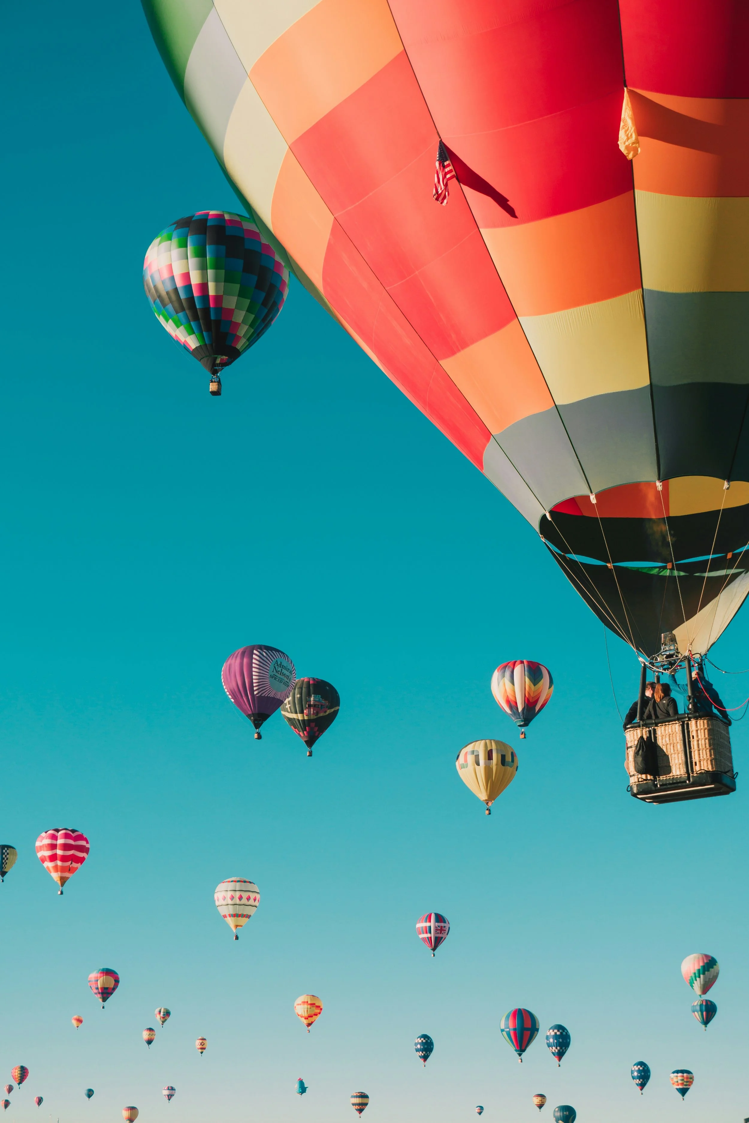 Multiple colorful hot air balloons floating in the sky, with one large balloon in the foreground and others scattered in the background against a clear blue sky.
