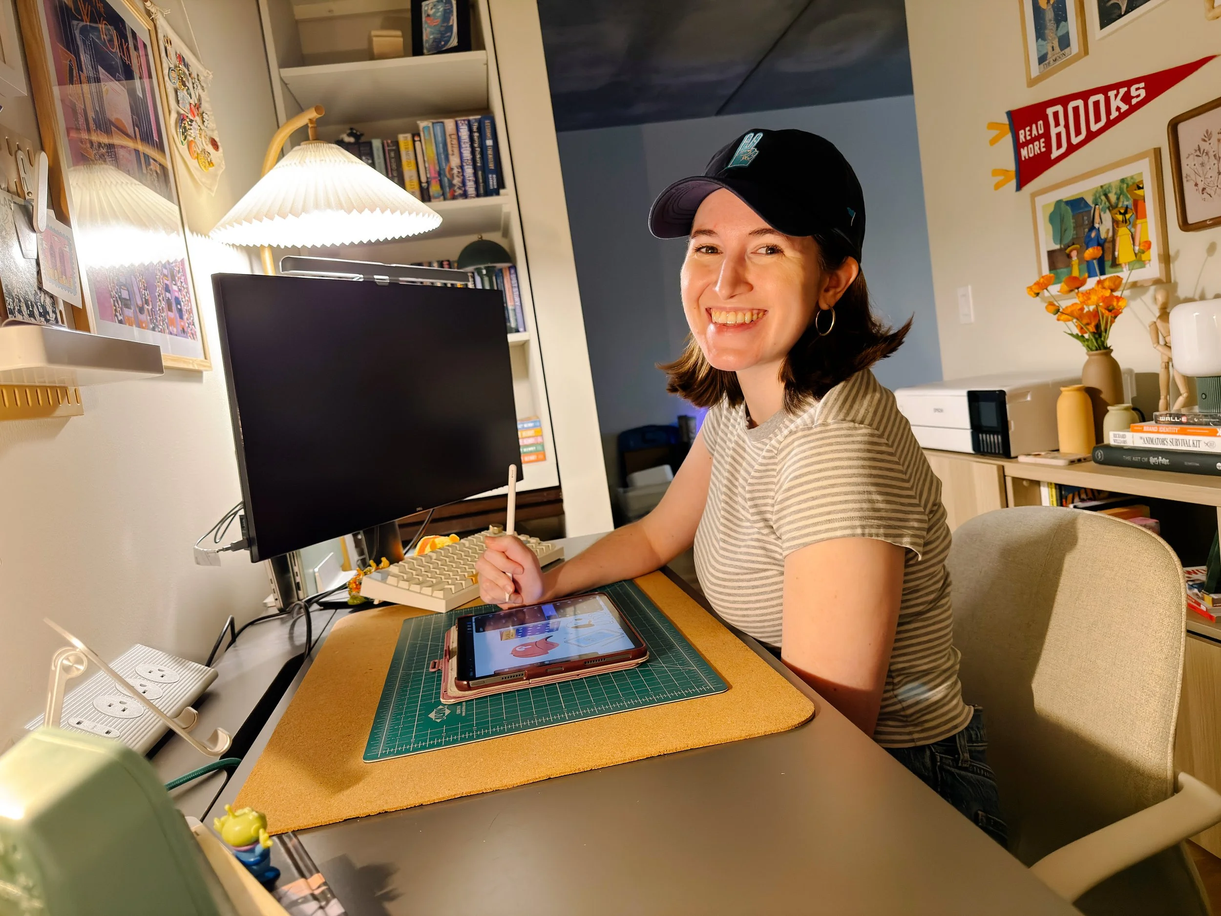 A woman smiling at a desk with a computer monitor, a tablet, and decorative items in a cozy home office.