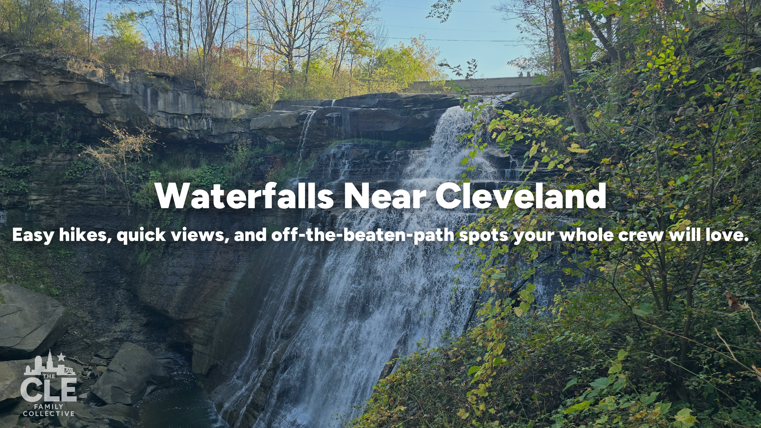 A waterfall near Cleveland flowing over rocks and surrounded by lush green trees, with a blue sky above.