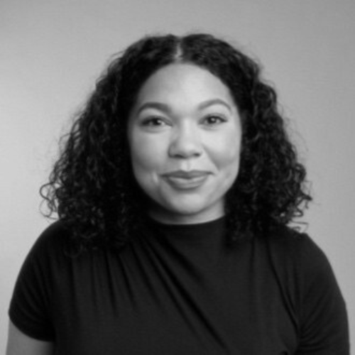 Portrait of a woman with curly hair, smiling, wearing a black top, against a plain background.