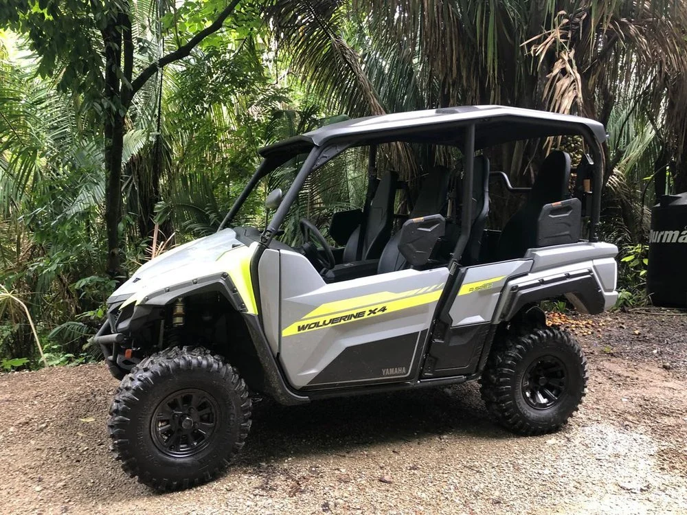 A Yamaha Wolverine X4 side-by-side utility vehicle parked on a dirt path surrounded by jungle foliage.
