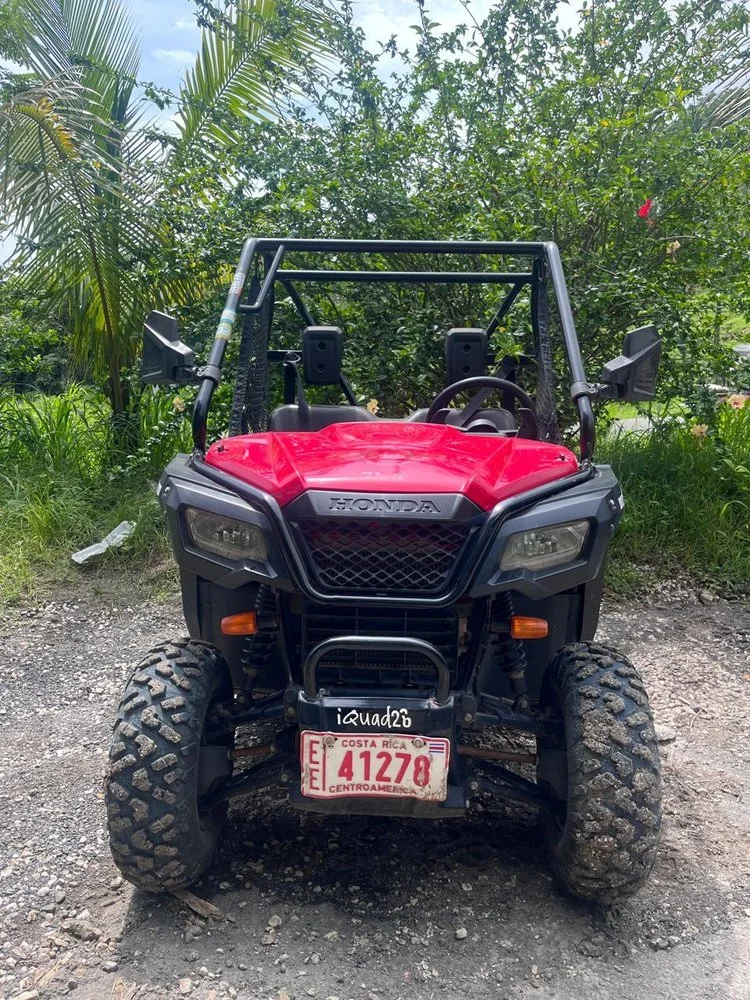 Red Honda off-road vehicle parked on a dirt path surrounded by lush green trees and plants.