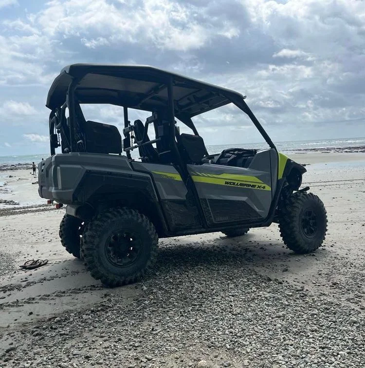 A gray off-road utility vehicle with black tires and a yellow stripe parked on a sandy beach with a cloudy sky.