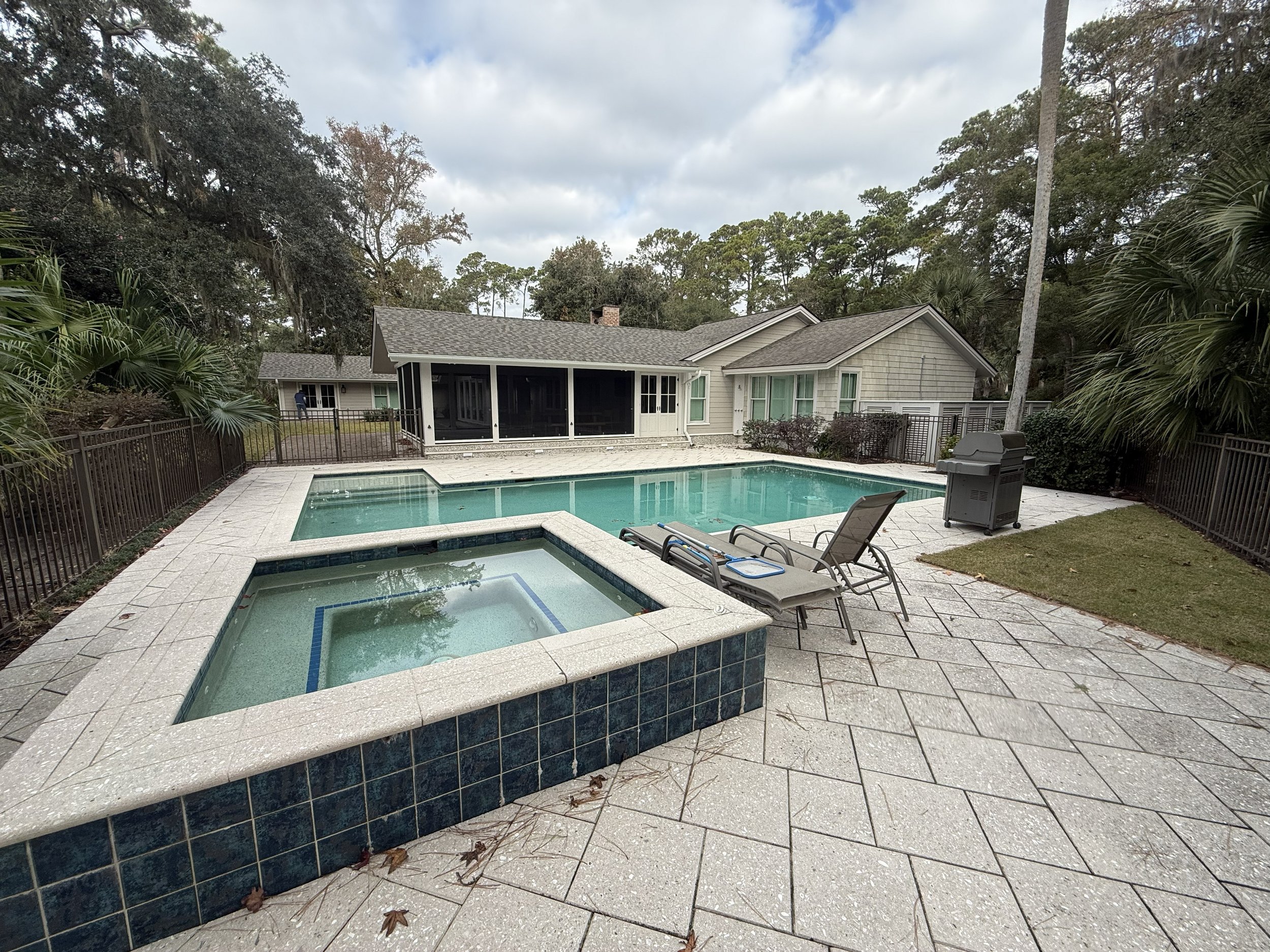 Backyard with a swimming pool, hot tub, patio chairs, surrounding trees, and a house with screened porch.