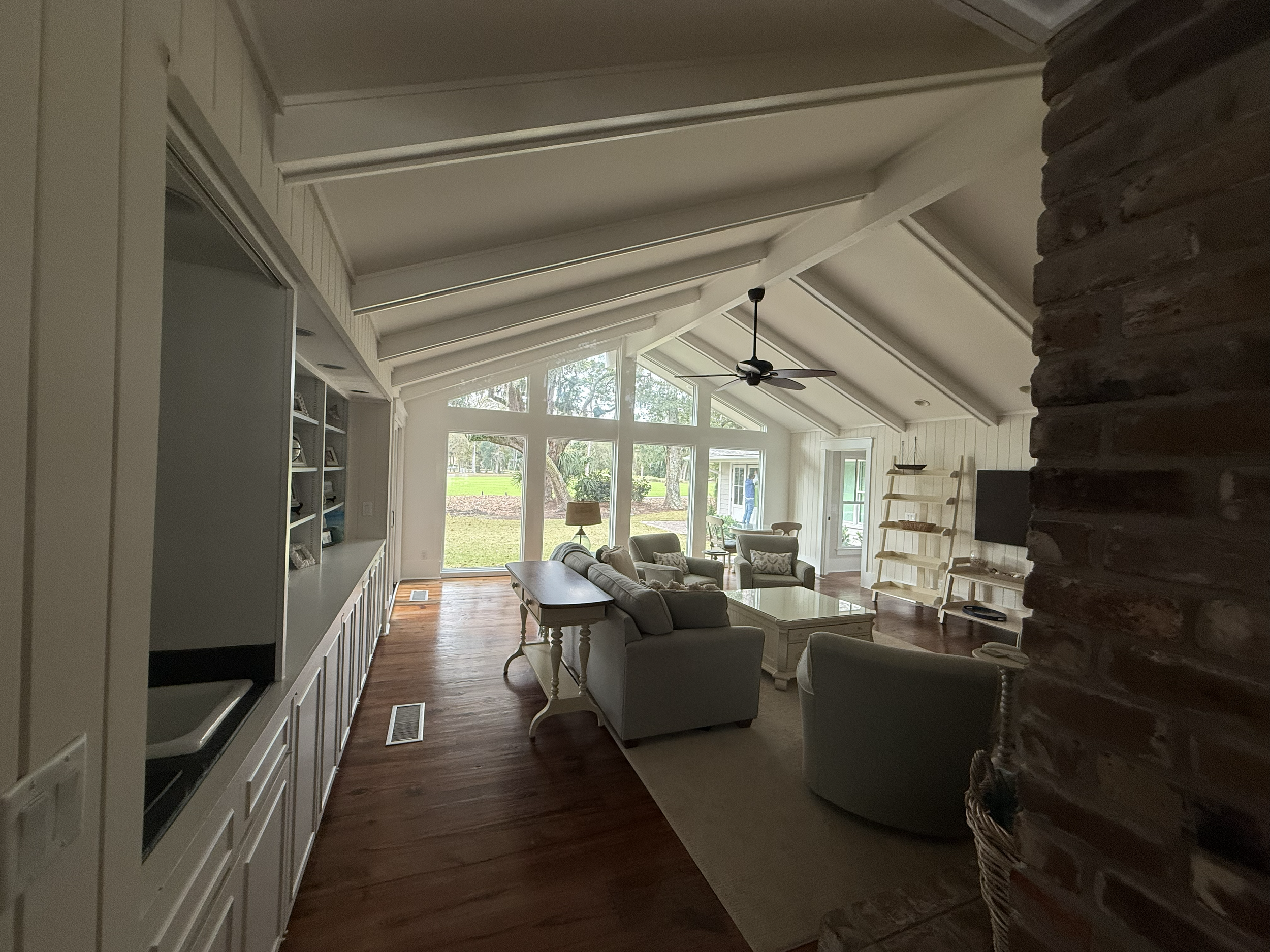Living room with white walls, large windows, a ceiling fan, and furniture including a sofa and chairs, with a view of outdoors.
