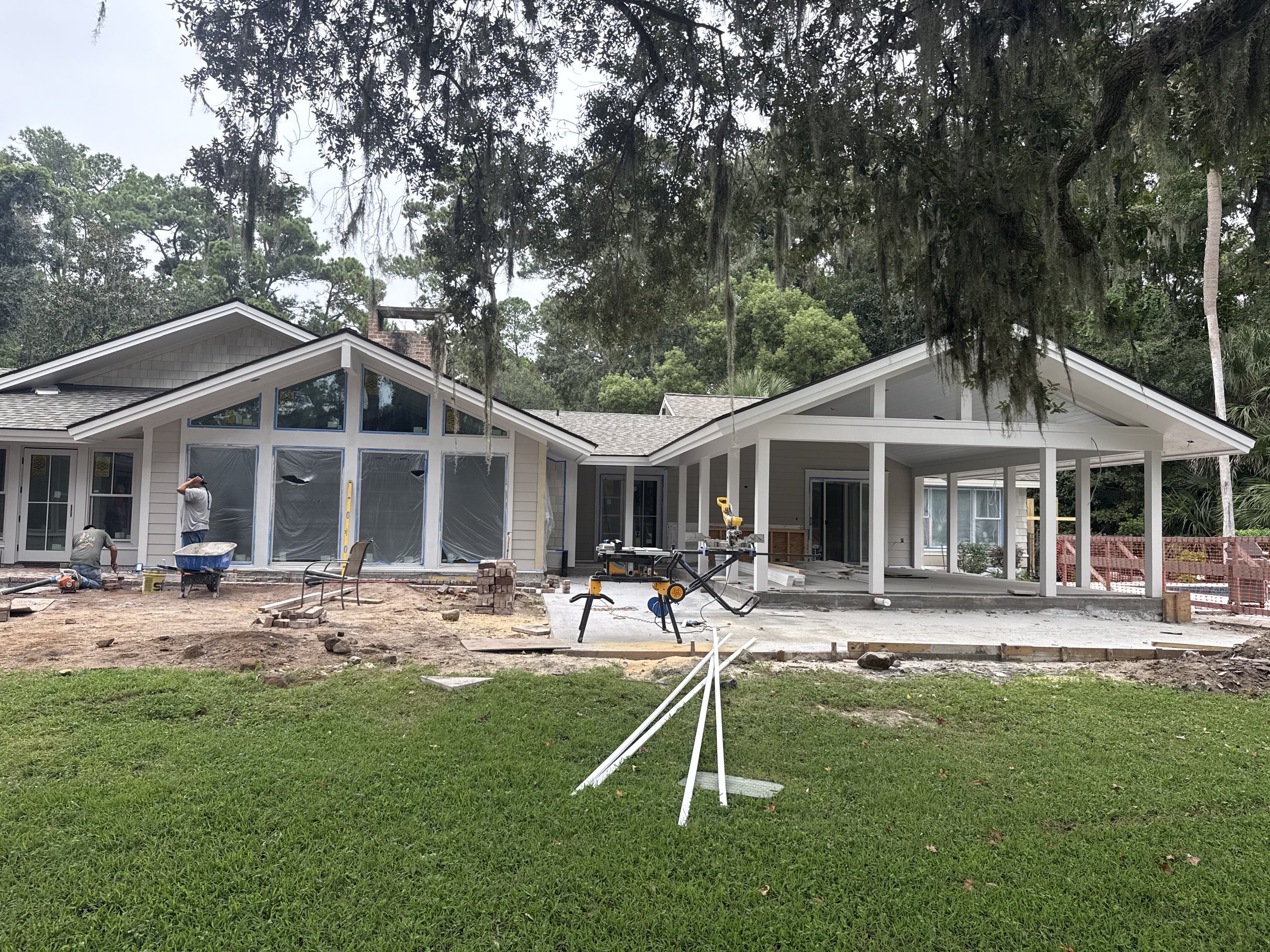 Construction site of a house with workers and tools, surrounded by trees and grass, as the house is being built or renovated.