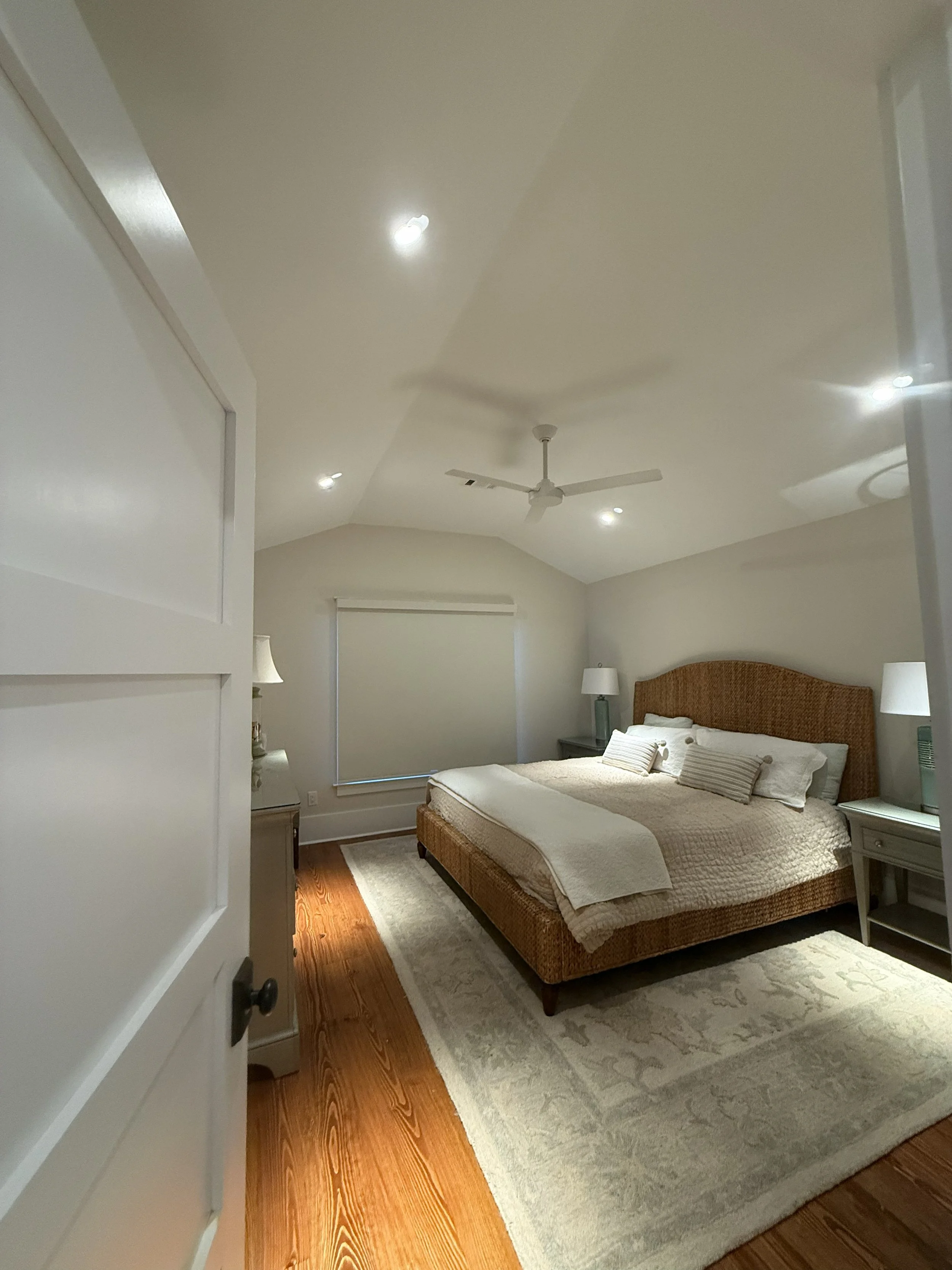A bedroom with a bed, side tables, lamps, and a ceiling fan, viewed from doorway.