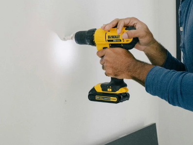Person using a yellow DeWalt cordless drill to drill into a wall.
