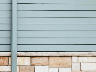 Close-up of a building exterior wall showing horizontal gray siding and a stone foundation.
