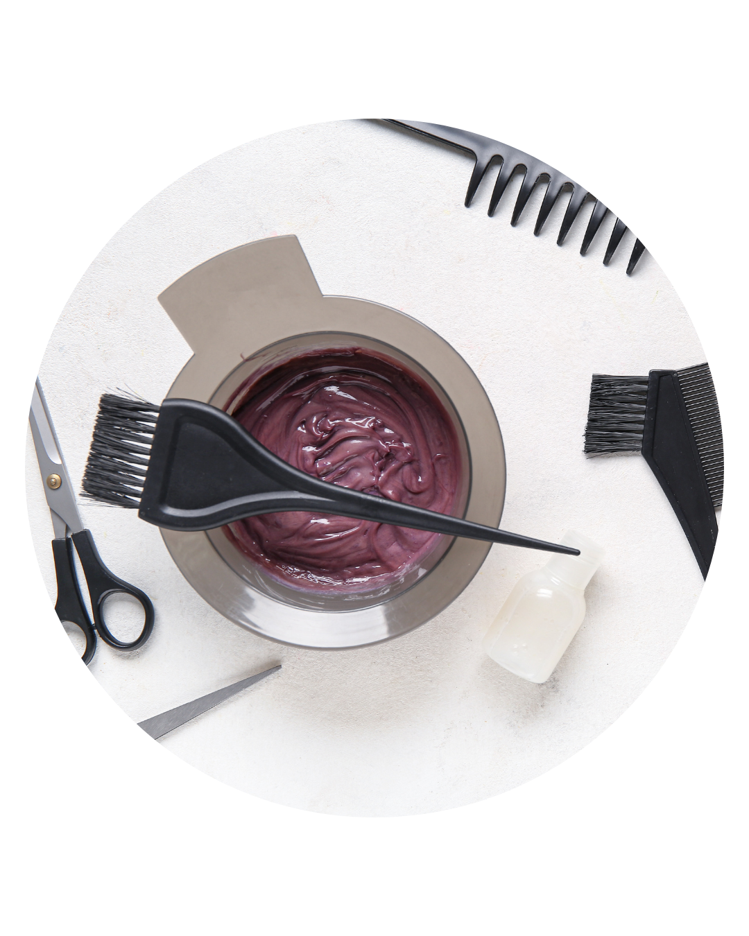 Hair dye mixture in a bowl with hairbrush, scissors, and combs on a white surface.