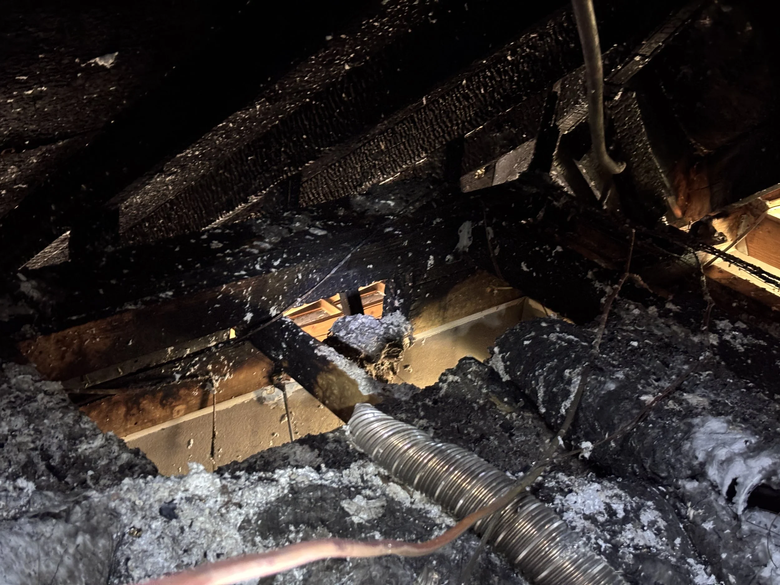 Charred attic with burnt insulation, blackened wooden beams, and damaged wiring after a fire. Fire damage to an attic. Fire Claims