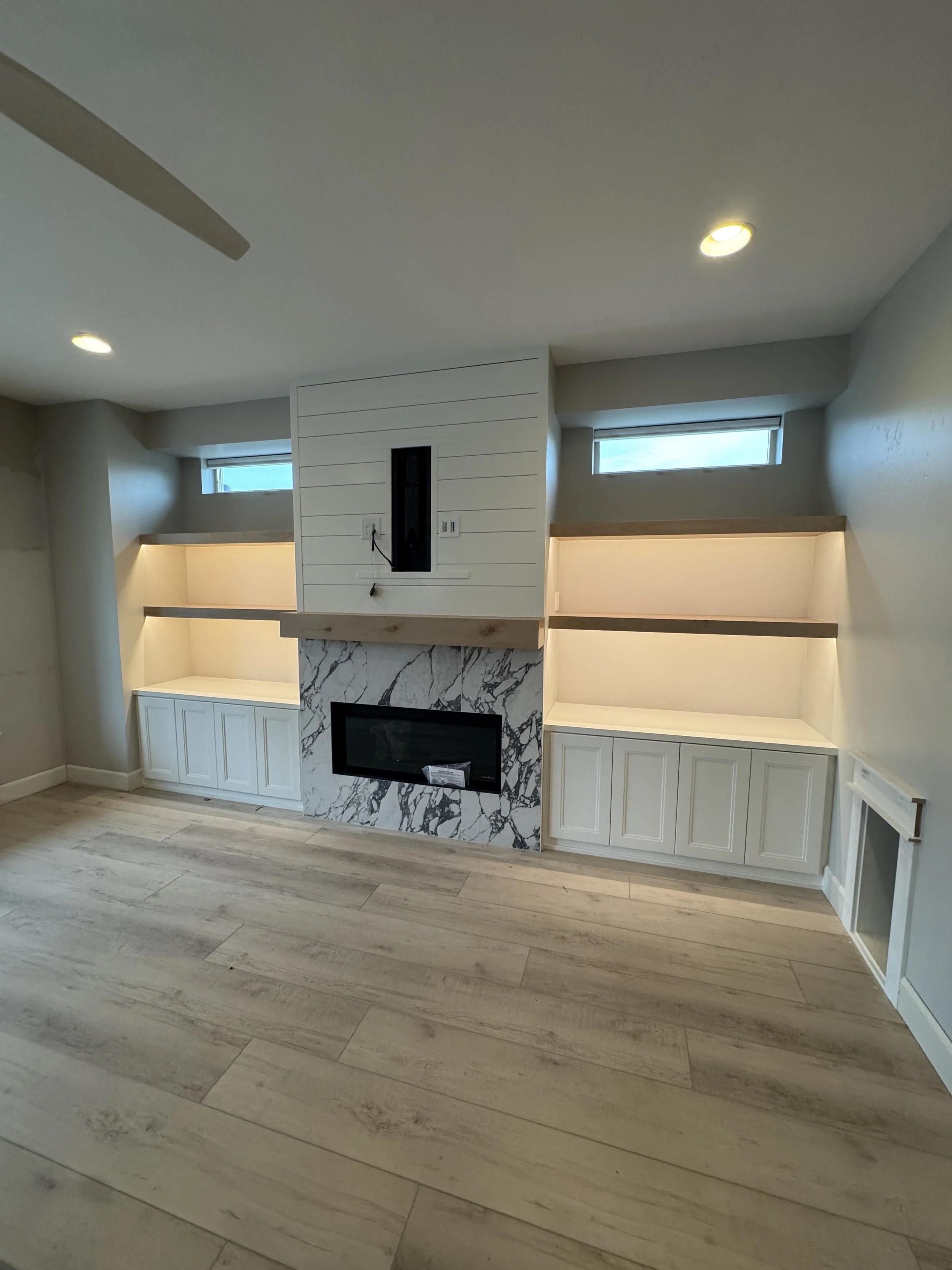 Living room with built-in white cabinets, a marble fireplace, and two small horizontal windows.