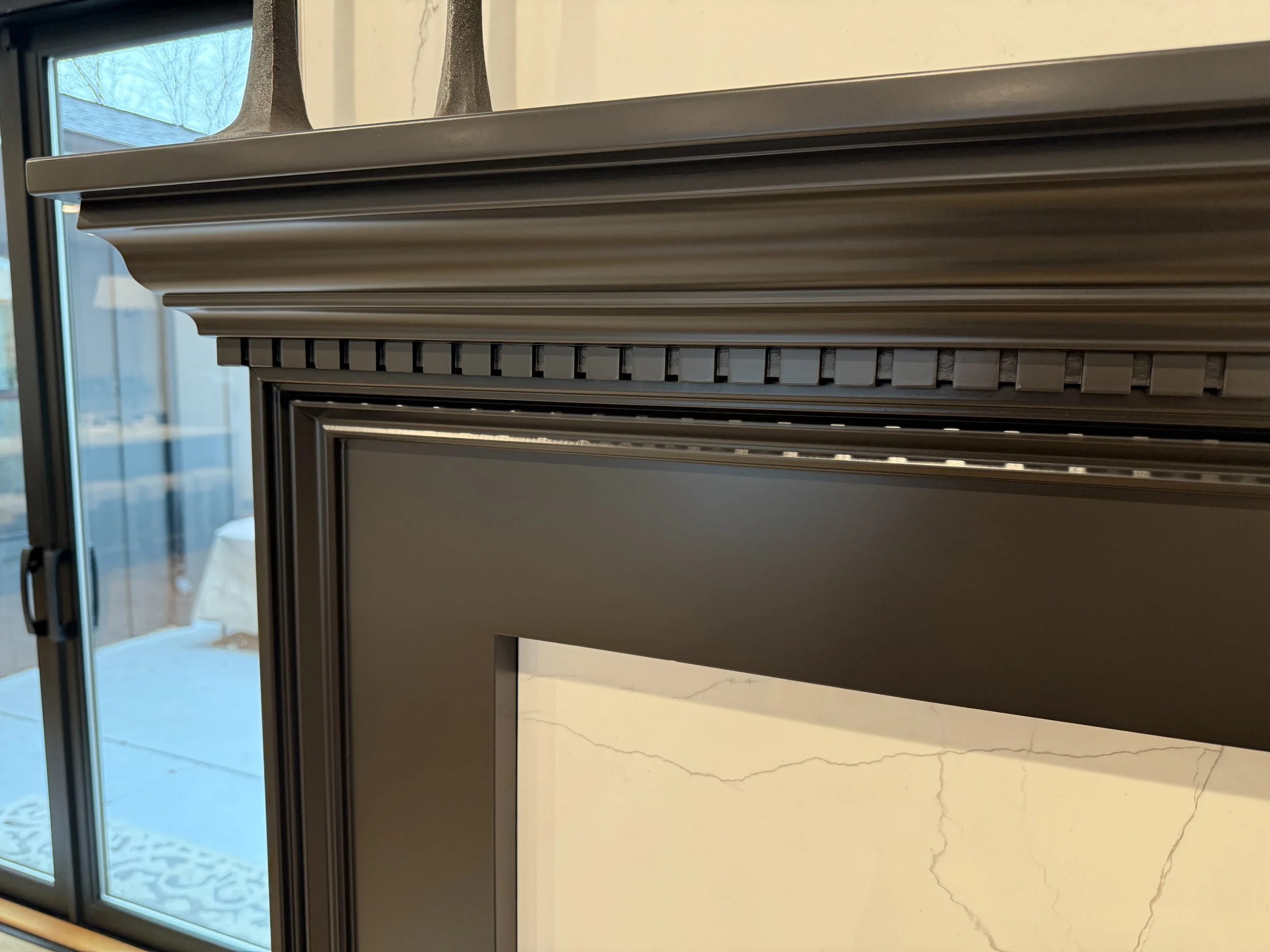 Close-up view of a dark-colored fireplace mantel with detailed molding, near a glass door.