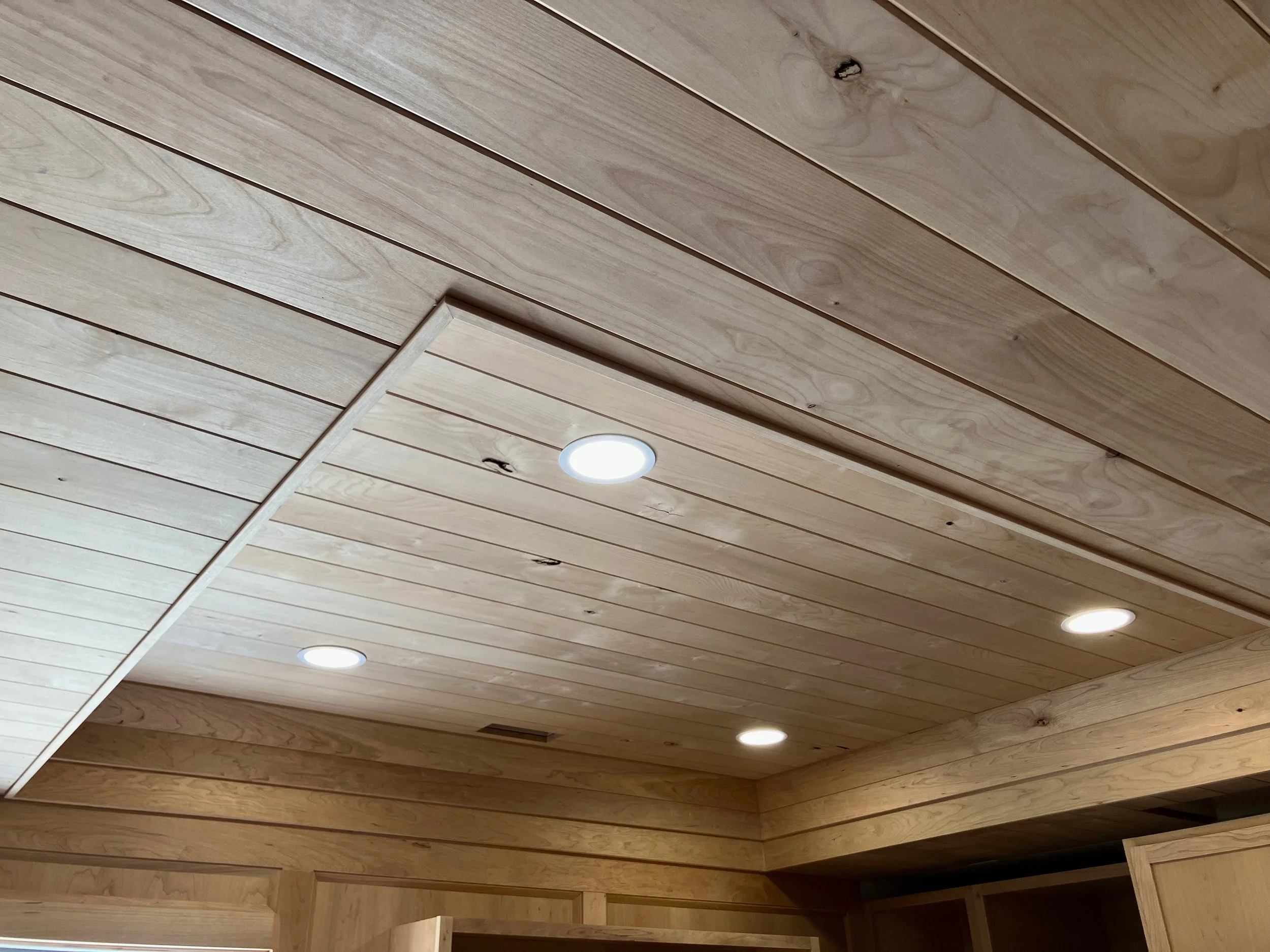 Ceiling made of light-colored wooden planks with four recessed lights and visible wood grains and knots in the panels.