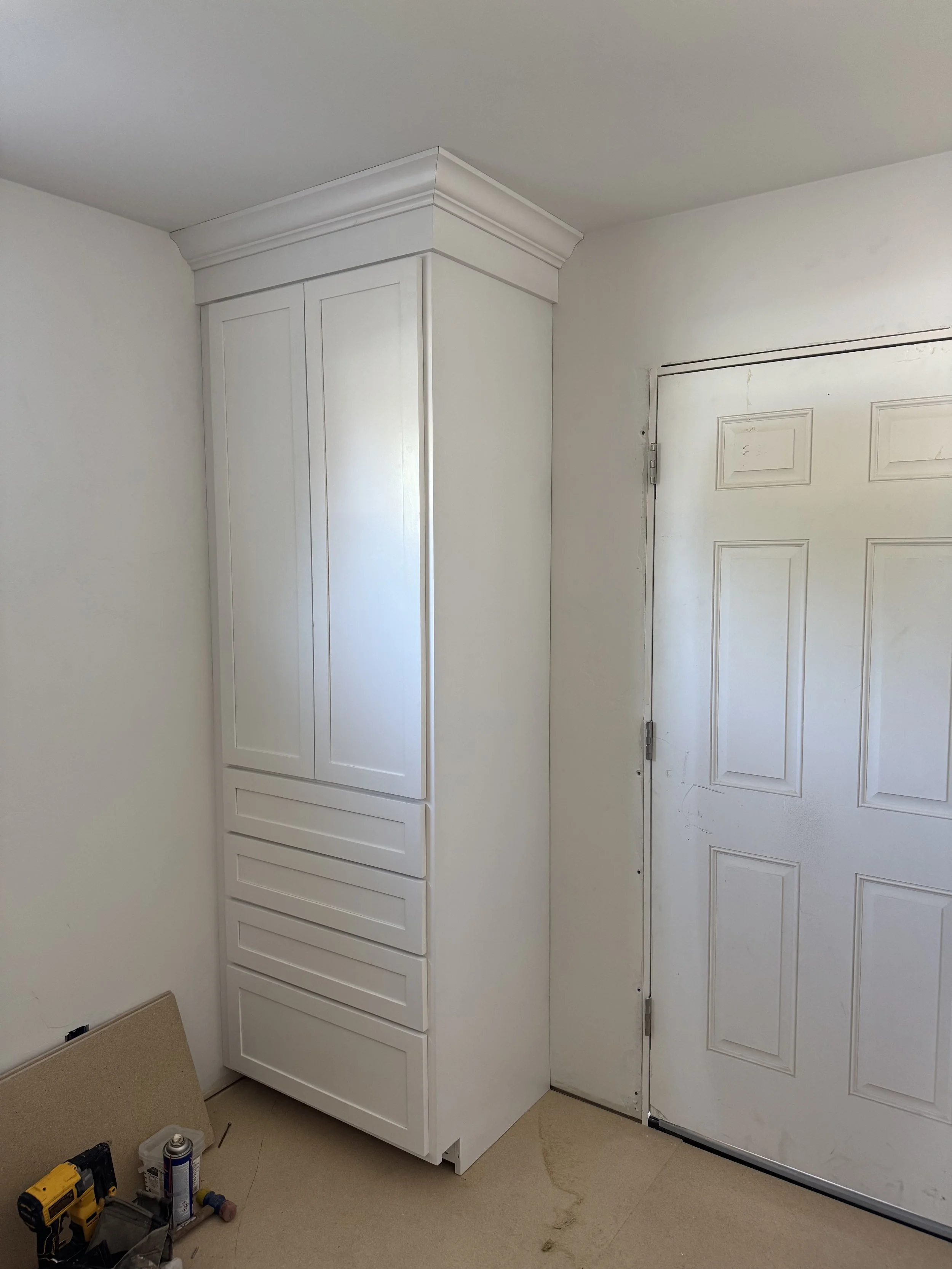 White corner cabinet with crown molding next to a white door in a room with beige carpet.