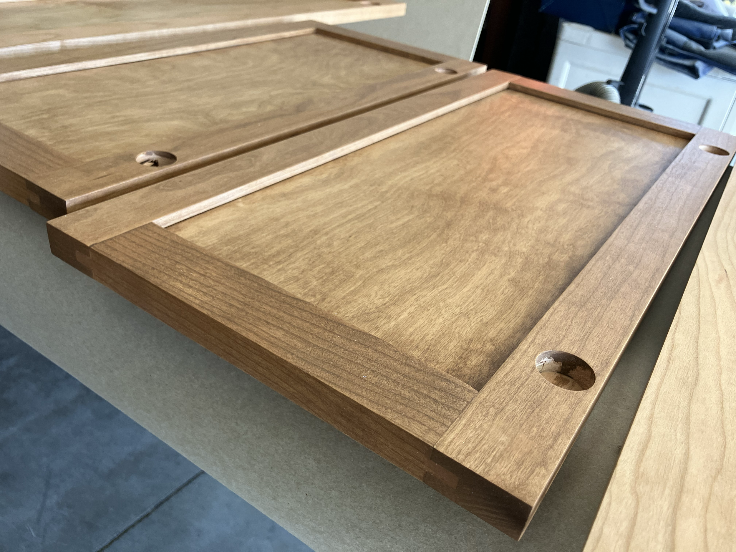 Two wooden trays with beveled edges and circular hole handles, placed on a beige surface.