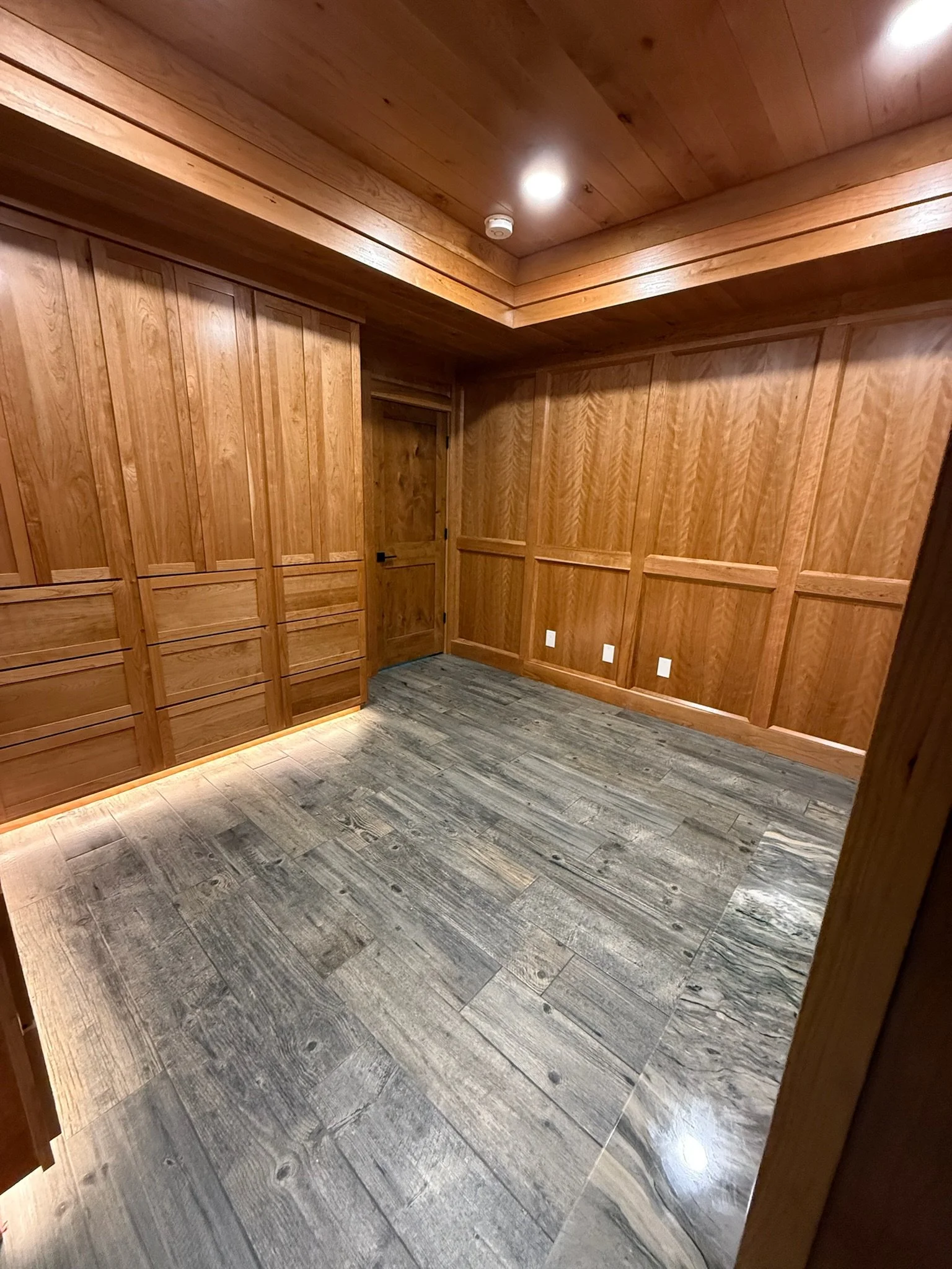 Empty room with wooden walls and ceiling, grey tile flooring, and electrical outlets.