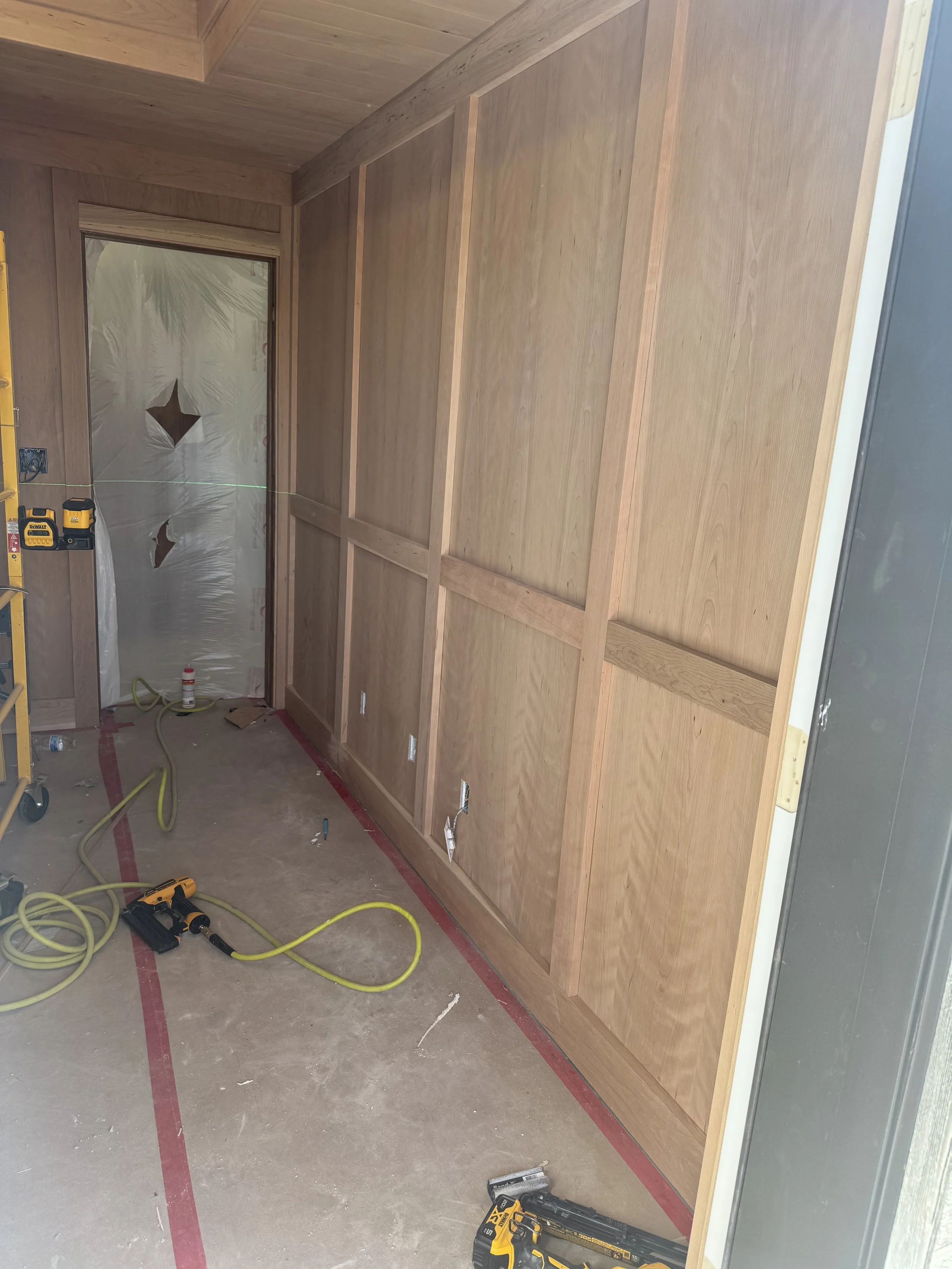 Interior of a room under construction with wooden wall panels, construction tools, and wiring visible on the floor.